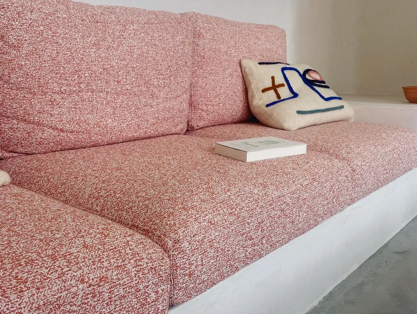 Canapé en tissu rose avec coussin décoratif, salon moderne lumineux, inspiration déco intérieure pour confort et style.