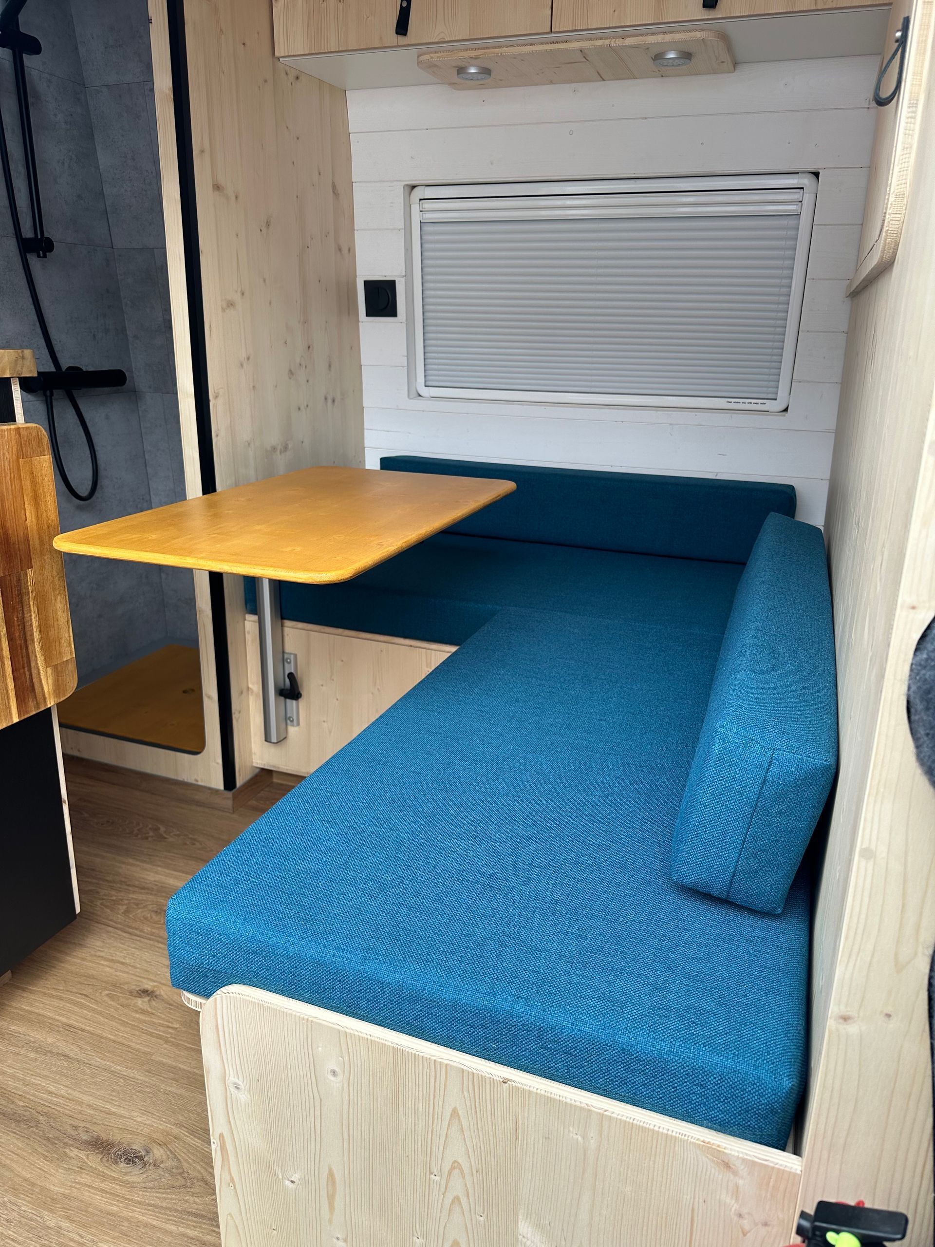 Banquette sur mesure bleu canard dans van aménagé avec plan de travail bois clair – coussin fourgon Mousse et Confection