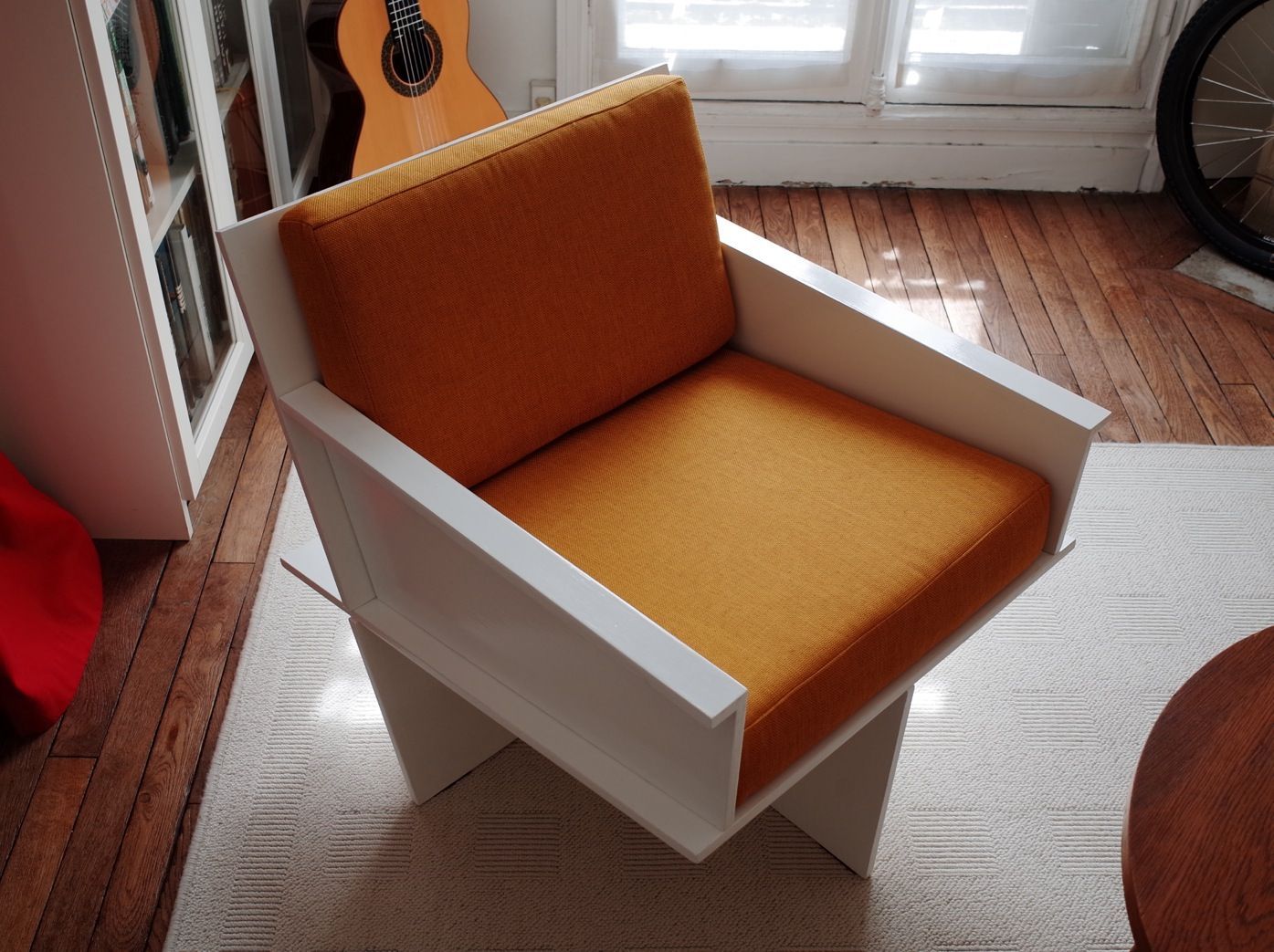 Coussin d'assise sur mesure en tissu orange pour la rénovation d'un fauteuil design en bois blanc.