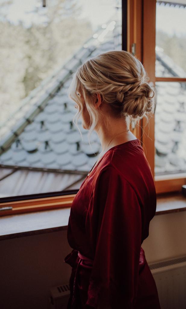 Hochsteckfrisur von hinten, geflochtener Dutt einer Braut am Fenster, elegantes Brautstyling
