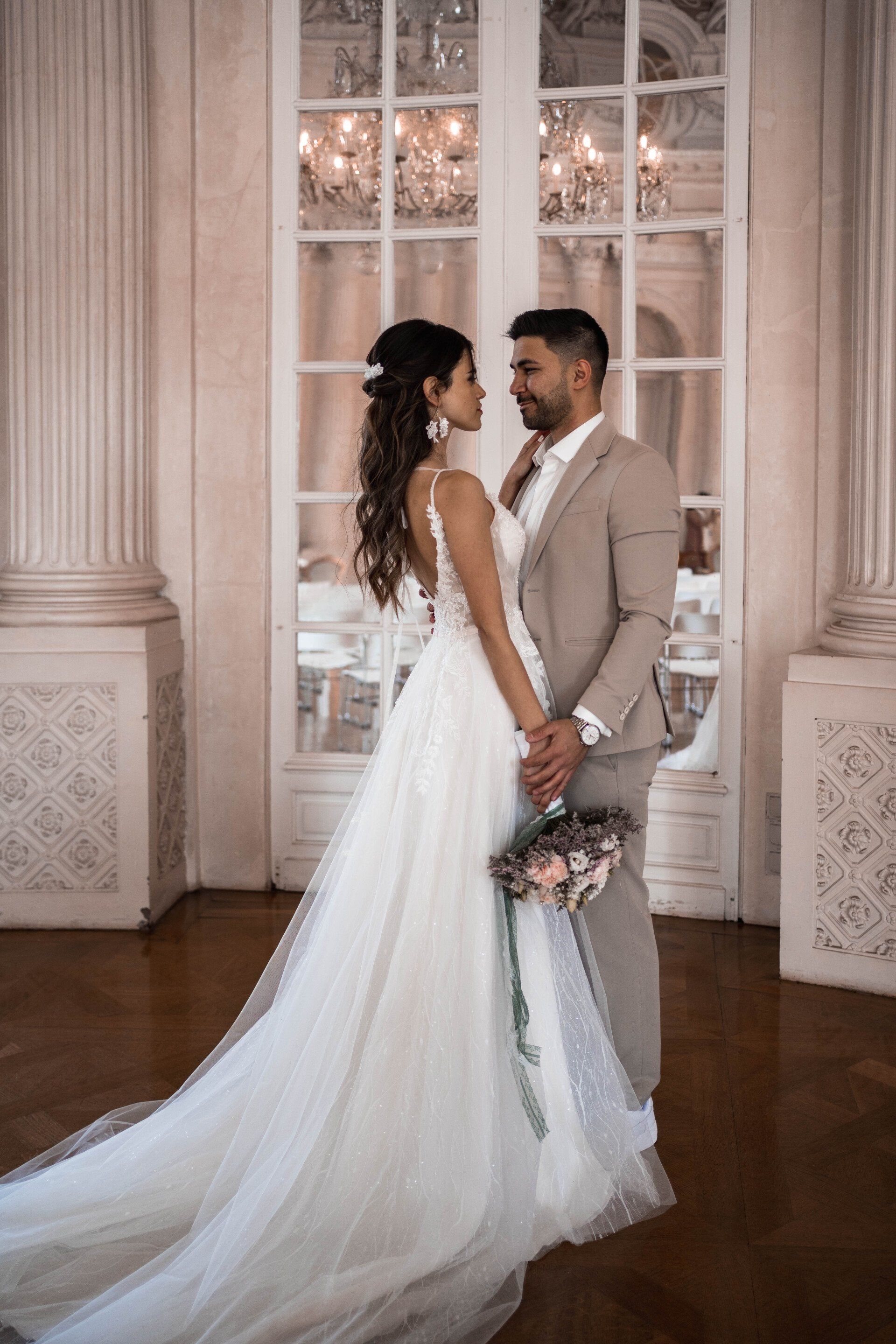 Brautpaar im eleganten Hochzeitssaal, Brautfrisur mit Haarschmuck und dezentes Braut-Make-up
