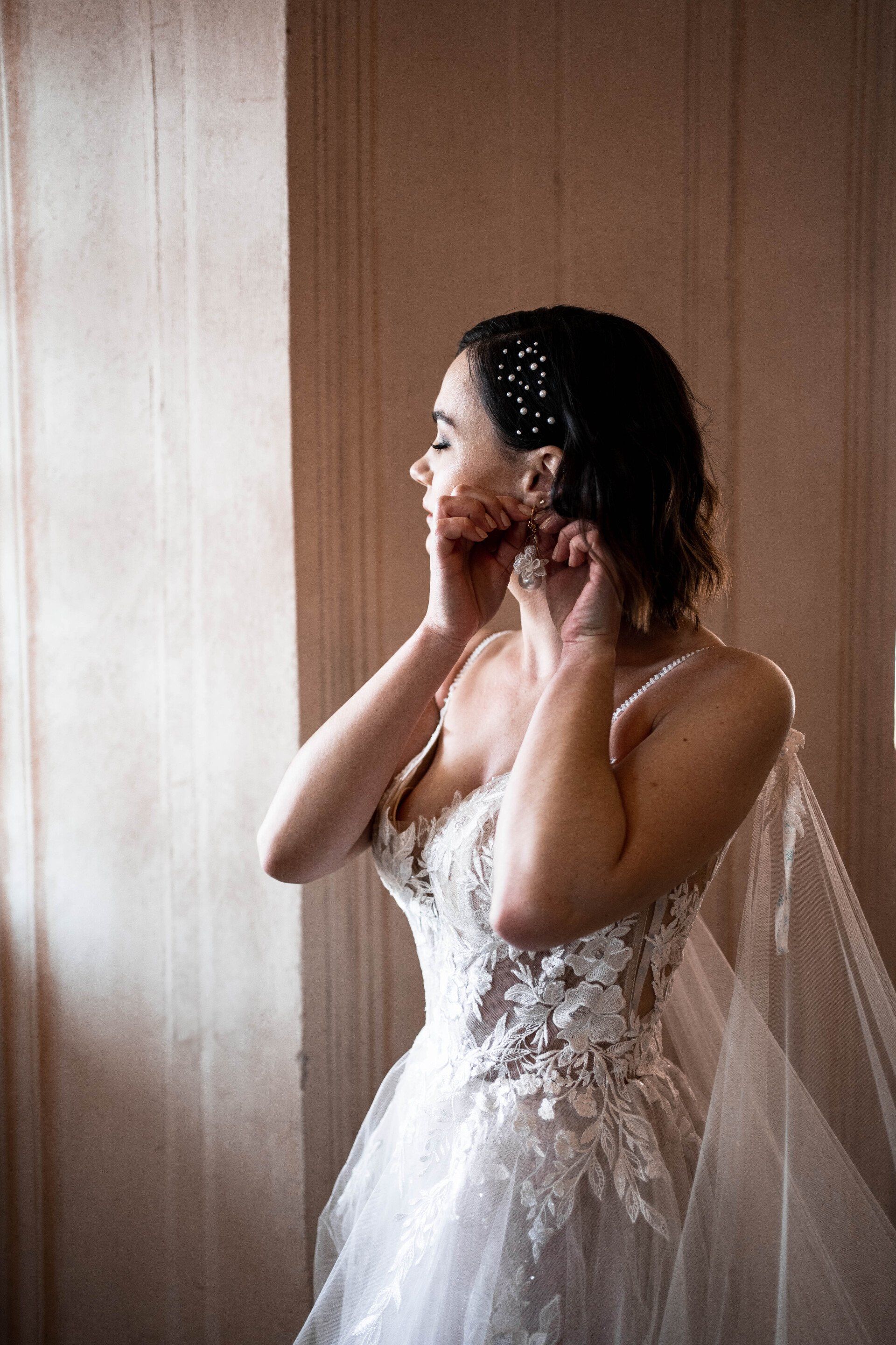 Seitliches Profil mit eleganter Brautfrisur, die Braut ist gerade dabei sich die Ohrringe anzulegen.