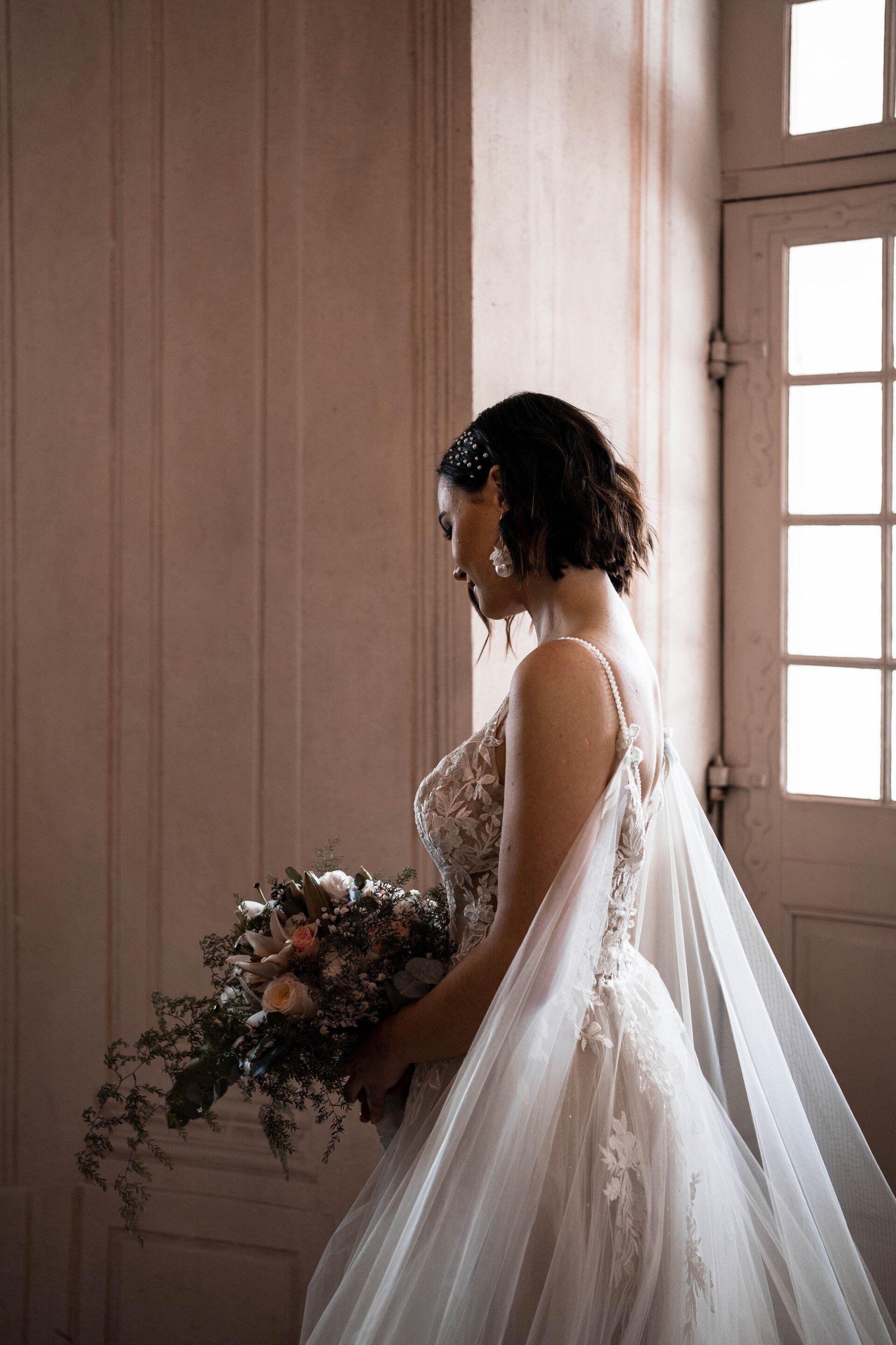 Dunkle Brautfrisur und elegantes Makeup, vor einem Fenster