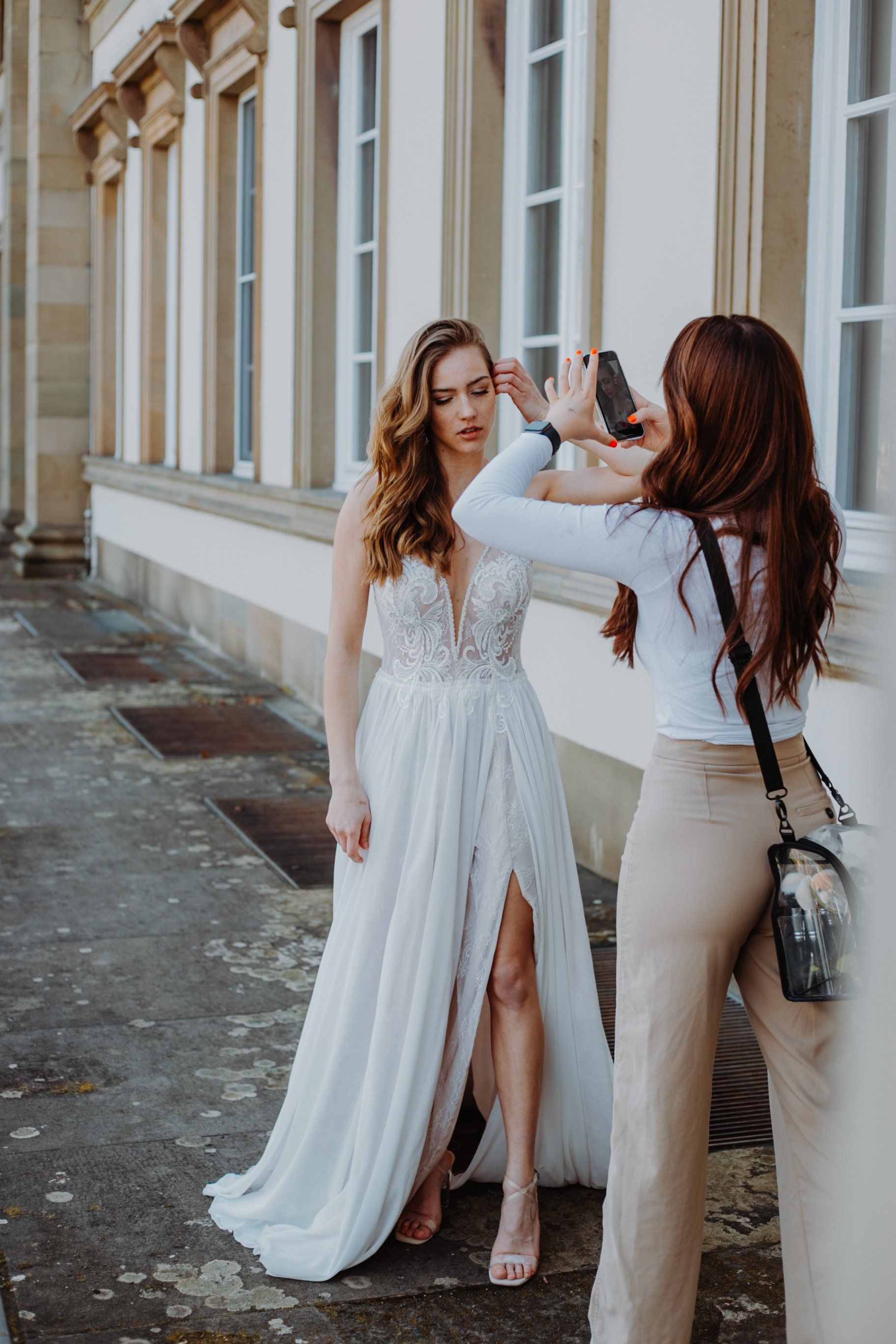 Brautstyling vor historischer Kulisse: Visagistin fixiert Braut-Make-up und Wellenfrisur am Hochzeitstag