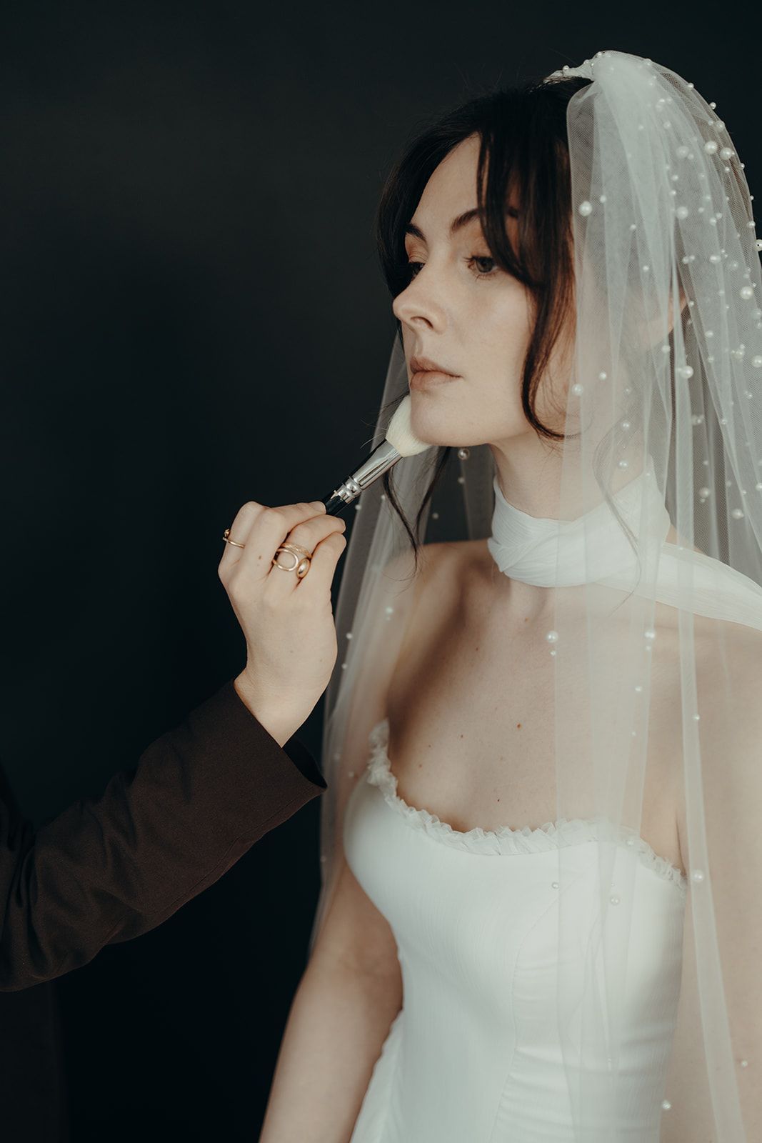 Brautporträt mit zartem Schleier und natürlichem Make-up vor dunklem Hintergrund.