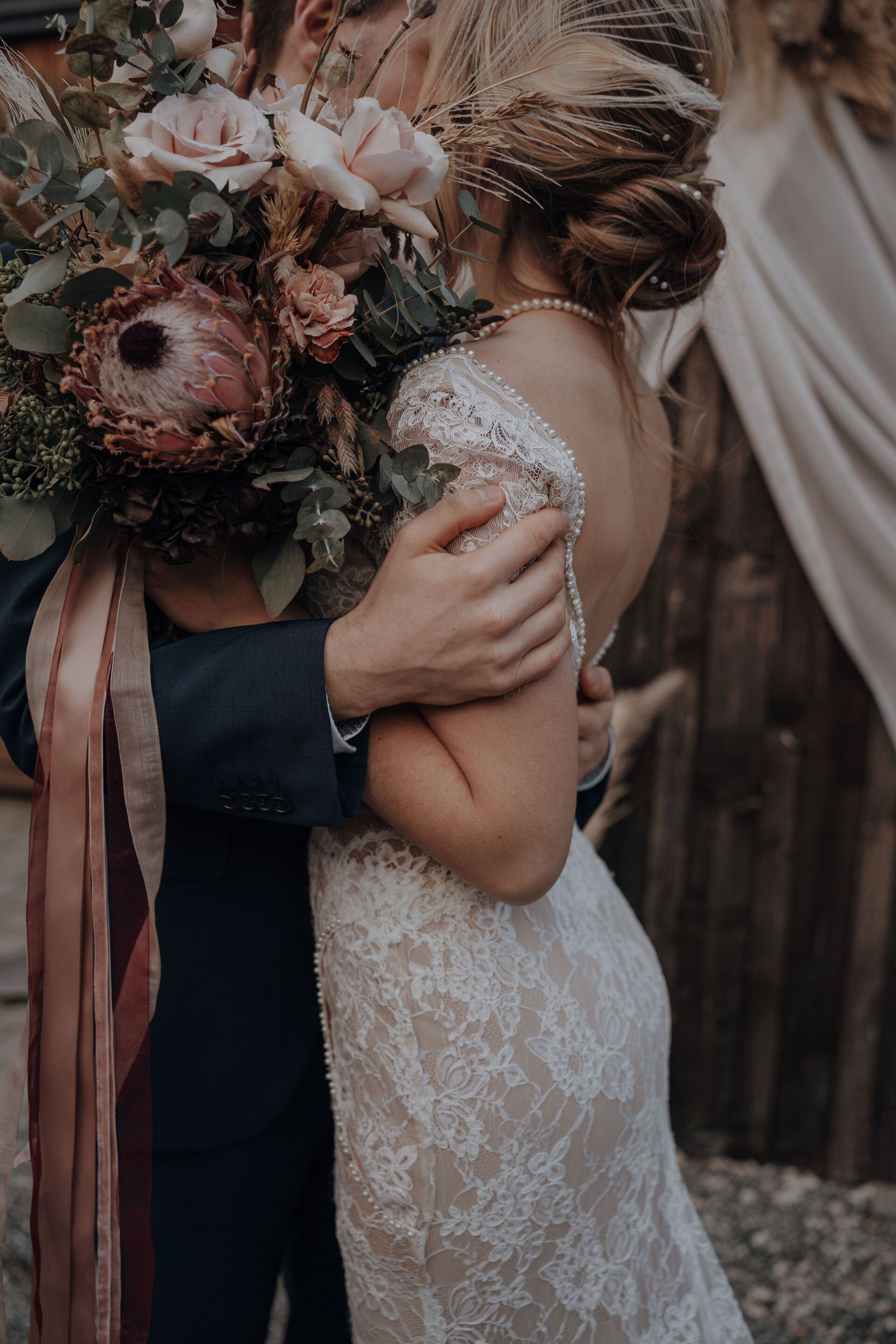 Elegante Braut küsst Bräutigam hinter den Hochzeitsblumen.
