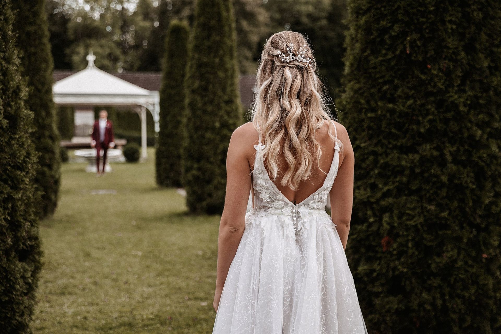 raut von hinten im Garten, lange lockige Brautfrisur und rückenfreies Hochzeitskleid