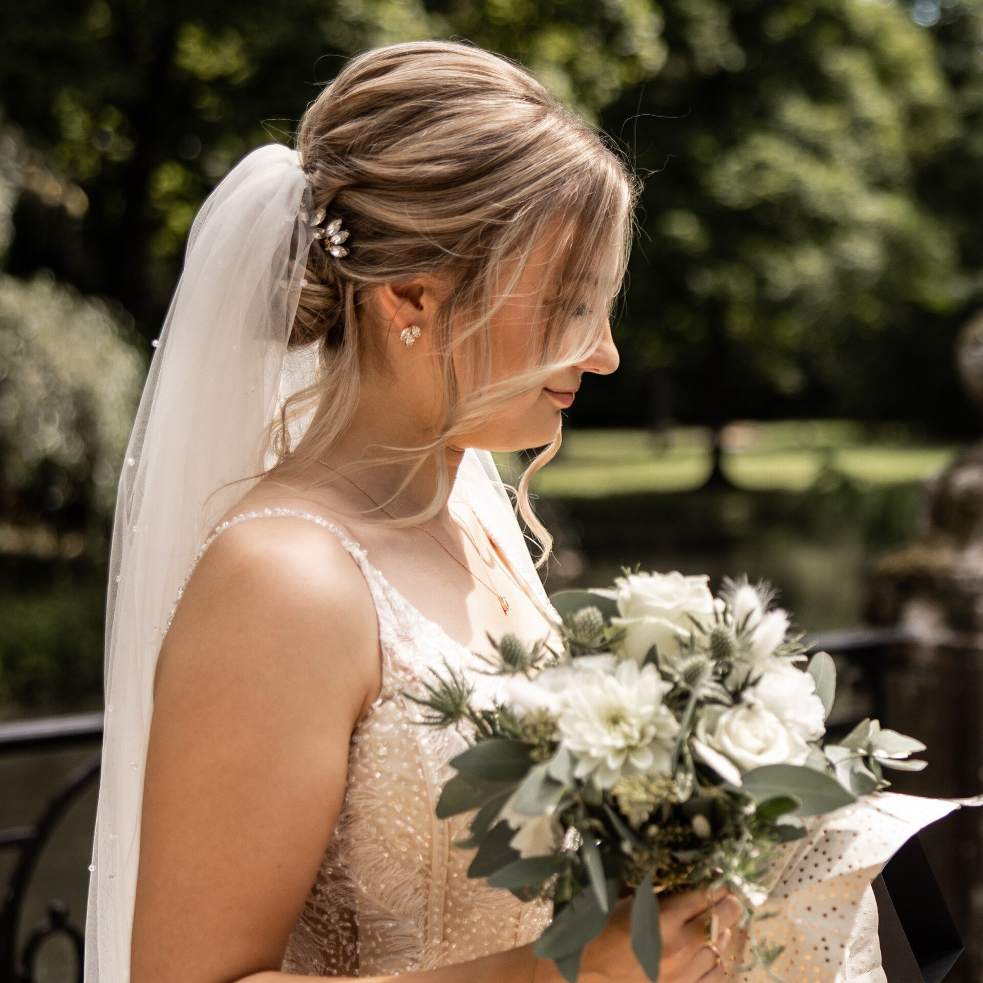 Braut mit elegant hochgesteckter Frisur, Schleier und natürlichem Make-up bei einer Sommerhochzeit im Freien.
