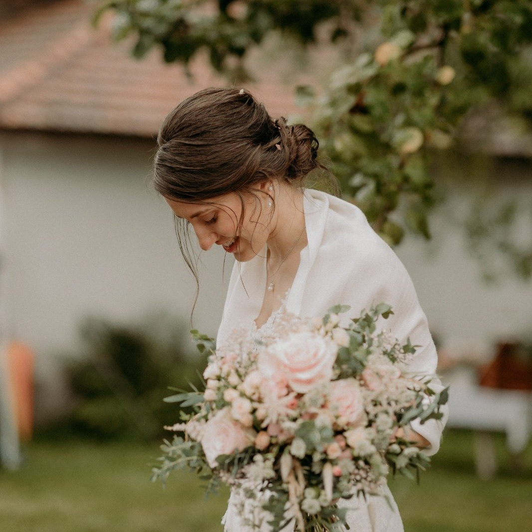 Braut mit lockerem, elegantem Low-Bun und natürlichem Make-up in einer Outdoor-Hochzeitskulisse.