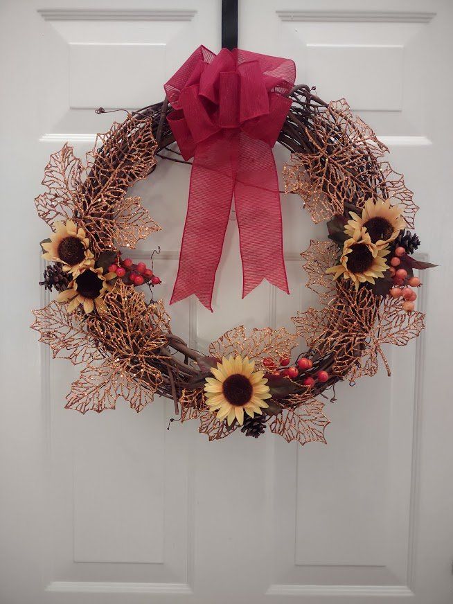 Grapevine wreath with berries, sunflowers, pine cones, and copper oversized leaves with a red bow.