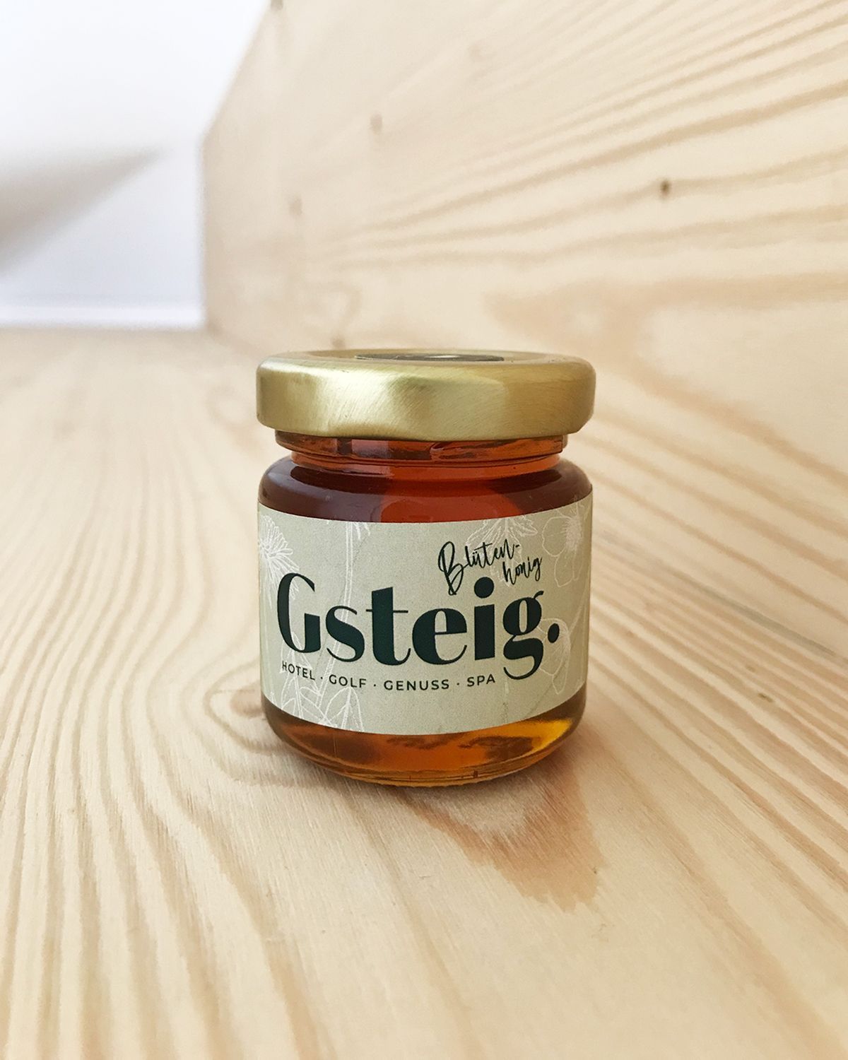 Produktfoto von einem 50ml Honigglas mit goldenem Deckel und Etikett für das Hotel Gsteig. in Lechbruck am See.