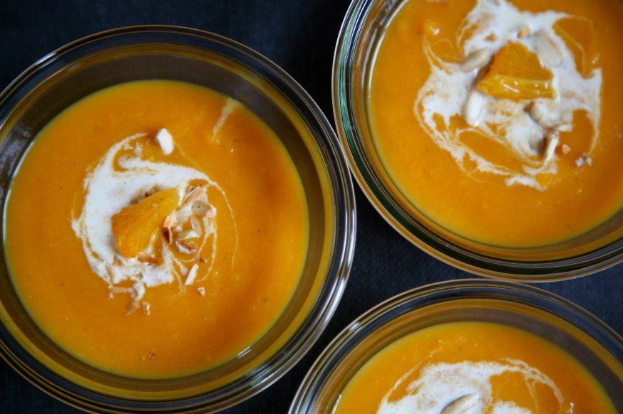 Drei Suppentassen von oben fotografiert. Darin ist eine Karotten-Orangensuppe mit Sahne Garnitur