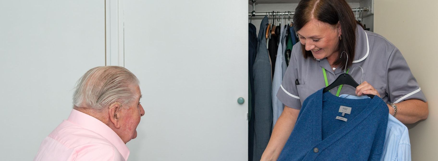 Gentleman being offered a blue cardigan by a carer.