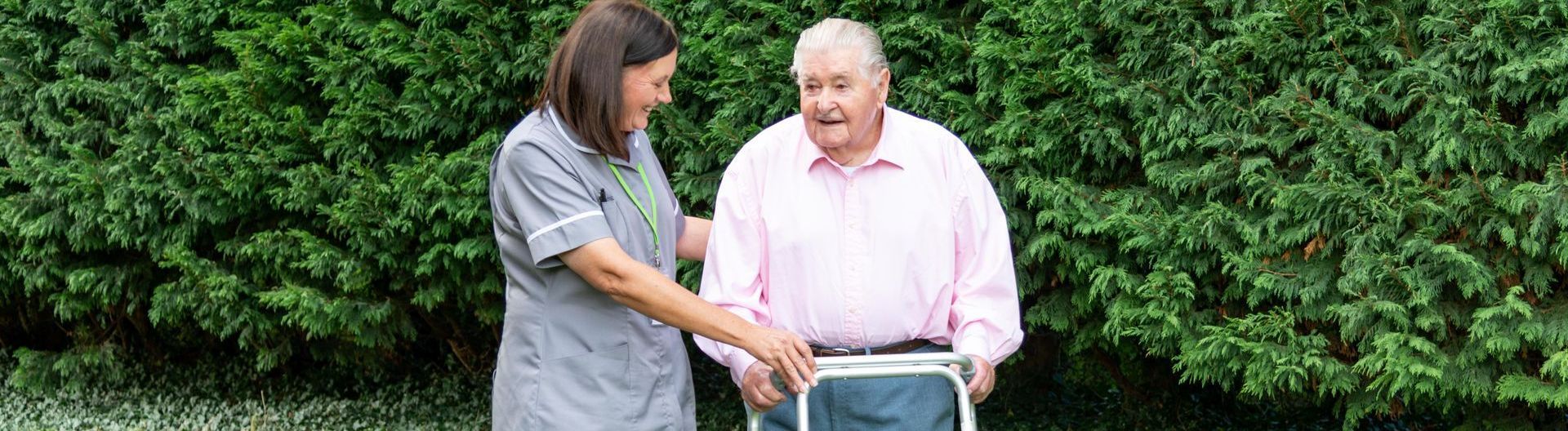 Gentleman assisted by a walking frame, chatting with a carer