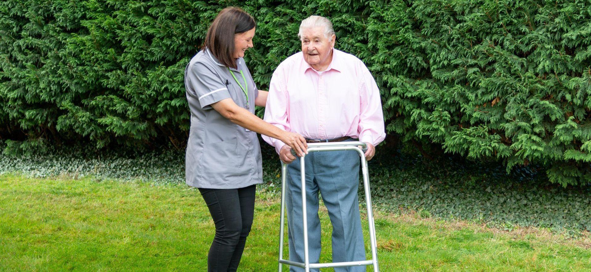 Gentleman assisted by a walking frame, chatting with a carer