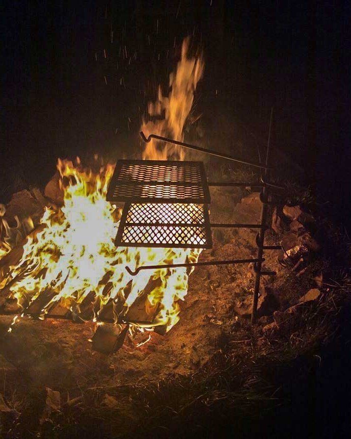 A close-up view of a clean grill grate positioned perfectly over glowing red campfire embers.