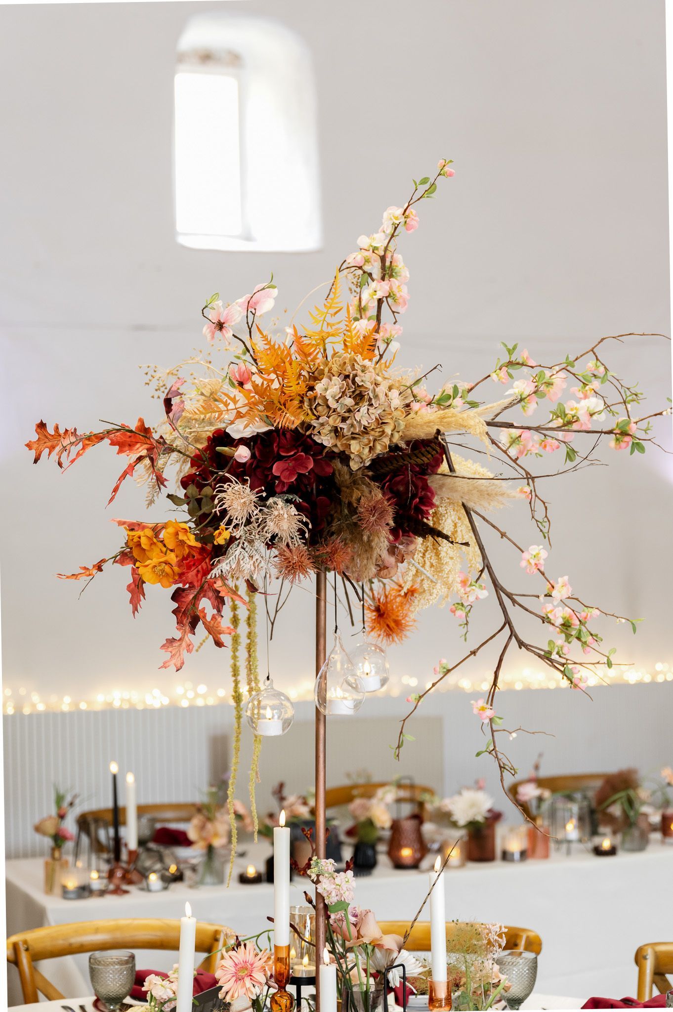 Hohe florale Tischdekoration in warmen Herbsttönen mit Kerzen und hängenden Glaswindlichtern im Historik Hotel Ebrach bei Bamberg – festgehalten von Thomas Freitag Fotografie.