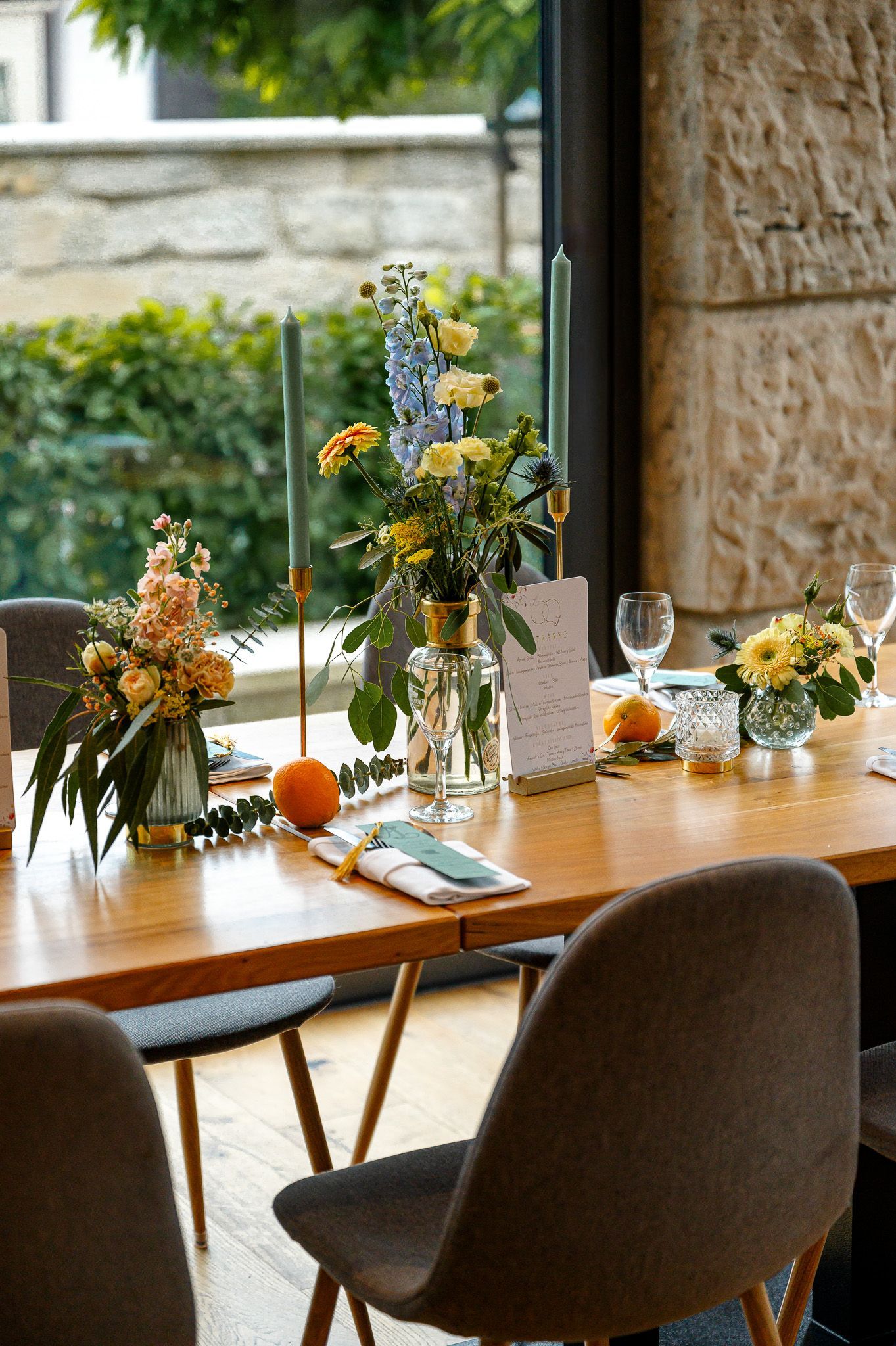 Übersicht einer festlich gedeckten Hochzeitstafel mit Blumenvasen, Kerzen, Menükarte und natürlichen Elementen wie Orangen und Eukalyptus