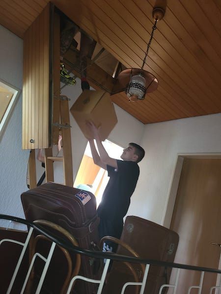 Ein Mann reicht einen Karton durch eine Dachbodenluke nach unten während einer Entrümpelung.