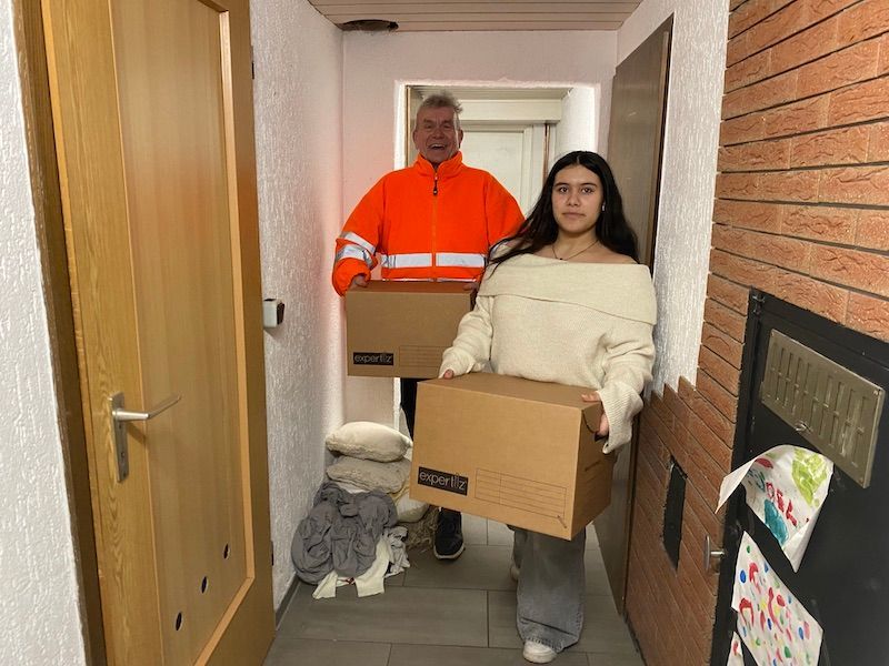 Zwei Personen tragen Umzugskartons aus einem Hausflur während einer Kellerentrümpelung.