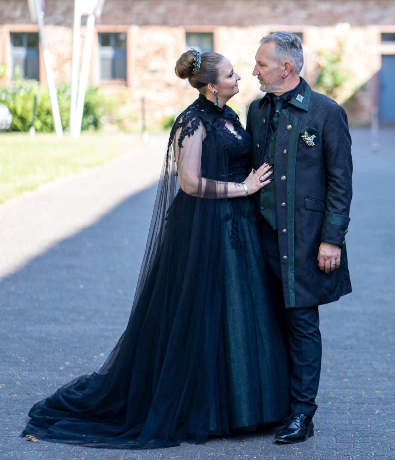 Elegantes Paar in perfekt aufeinander abgestimmten Dark Dream Collection Outfits: Die Frau trägt ein bodenlanges schwarzes Spitzenkleid mit transparenten Ärmeln und Cape, der Mann einen schwarzen Gehrock mit grünen Akzenten und Vintage-Brosche – beide blicken sich verliebt an und verkörpern zeitlose Eleganz mit Gothic-Flair.
Verliebt im viktorianischen Stil: Dieses Paar zeigt, wie eindrucksvoll und edel schwarze Gothic-Outfits von der Dark Dream Collection sein können – ideal für Hochzeit, Jubiläum oder ein exklusives Event.
