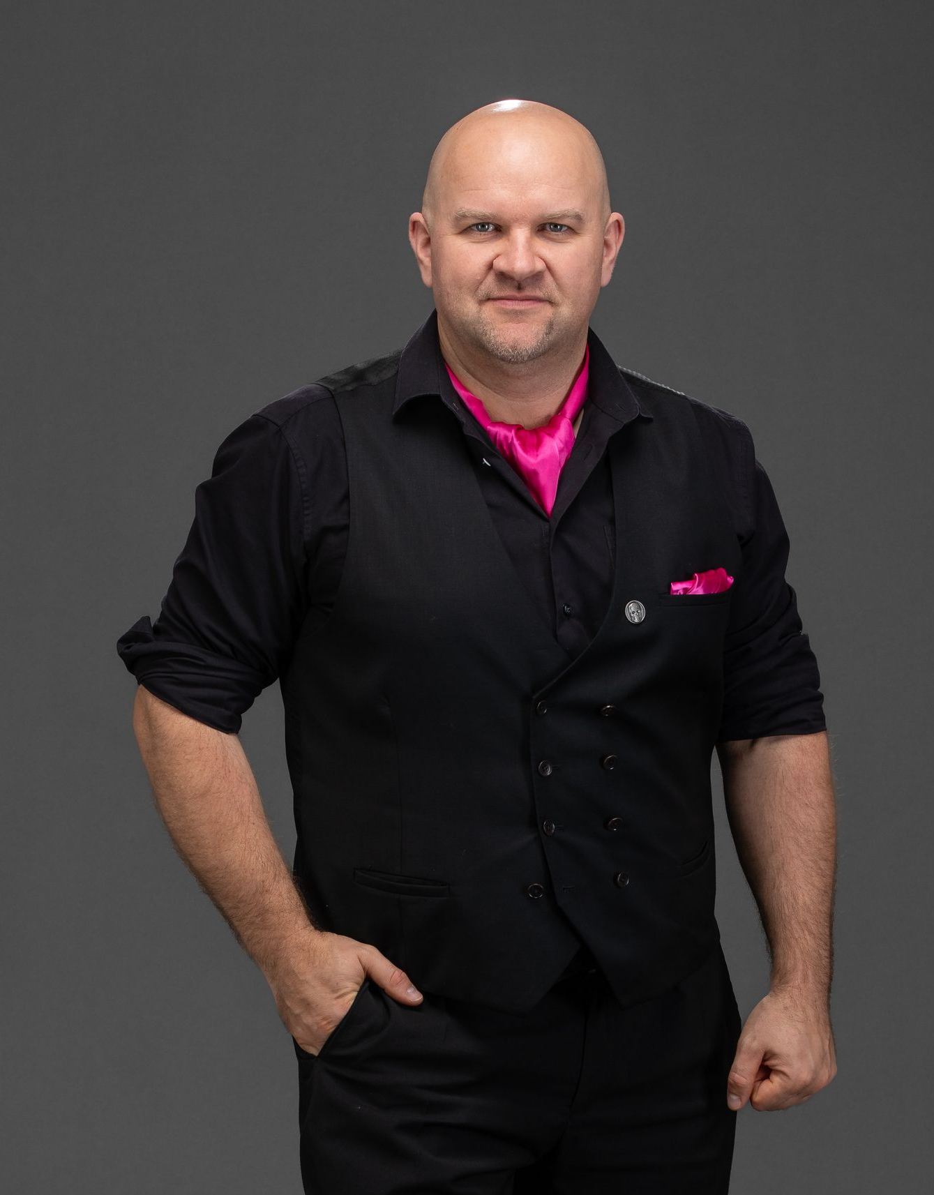 Gerhard Hübner, Mitgründer der Dark Dream Collection, im schwarzen Outfit mit Weste und pinkem Einstecktuch im Studio porträtiert.