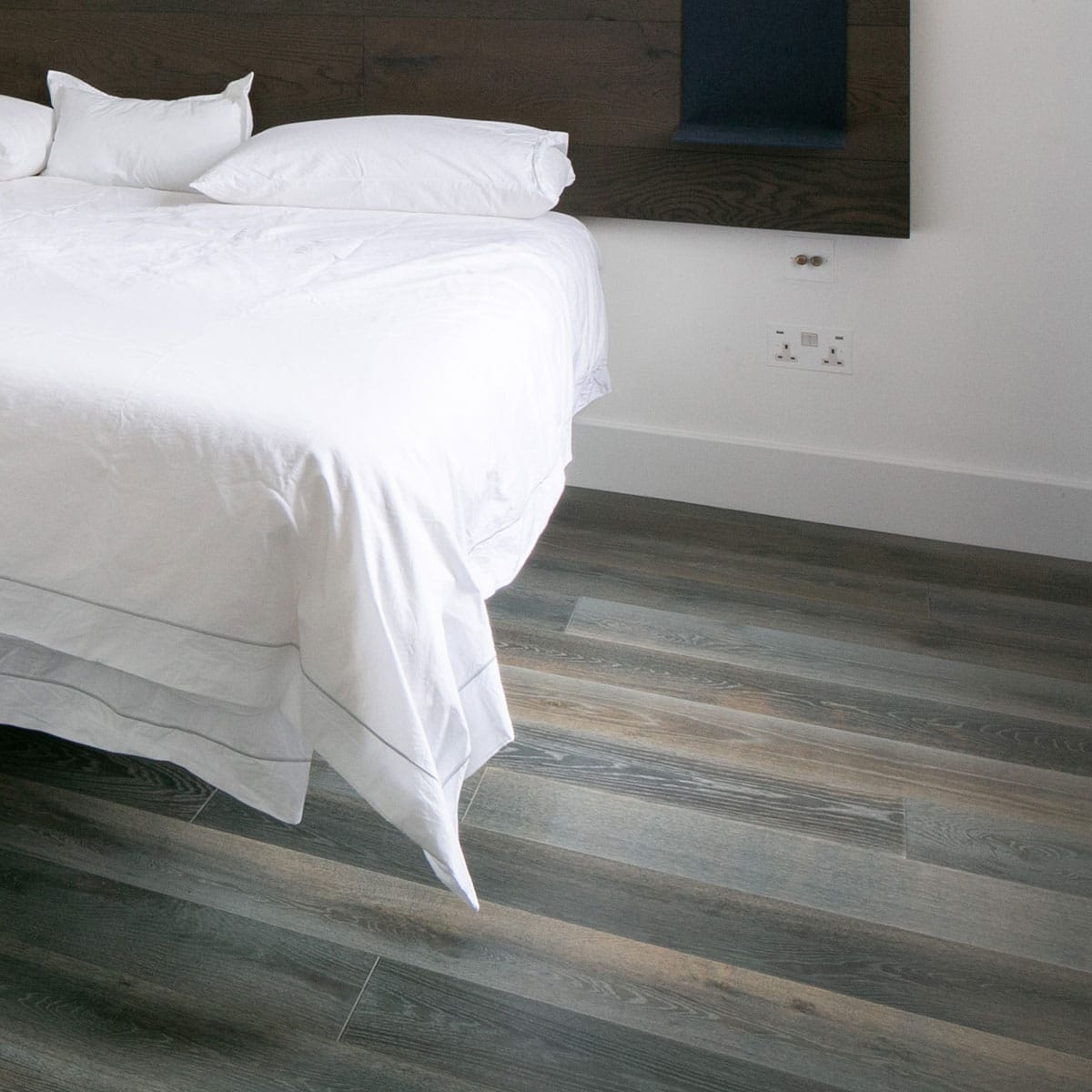 Grey oak effect laminate floor in a bedroom bed with white bed covers