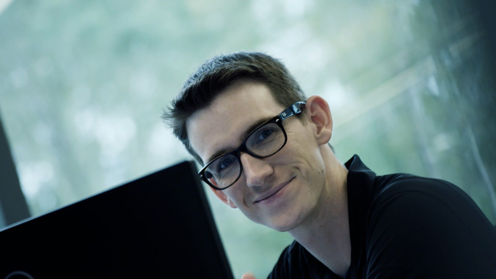 Smiling person behind a desktop monitor