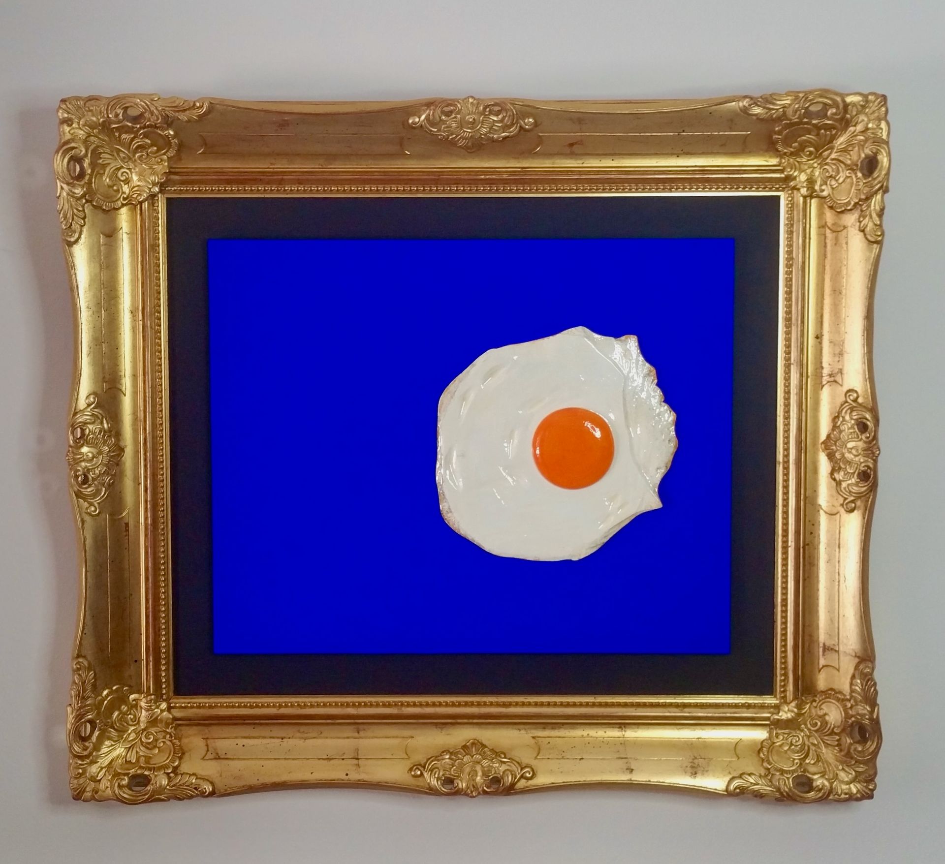 Das Bild zeigt ein Spieglei auf einem blauen Grund im Goldrahmen. Ein beliebtes Motiv von Bildhauer Oliver Pohl aus Haste im Schaumburger Land in der Nähe von Bad Nenndorf.