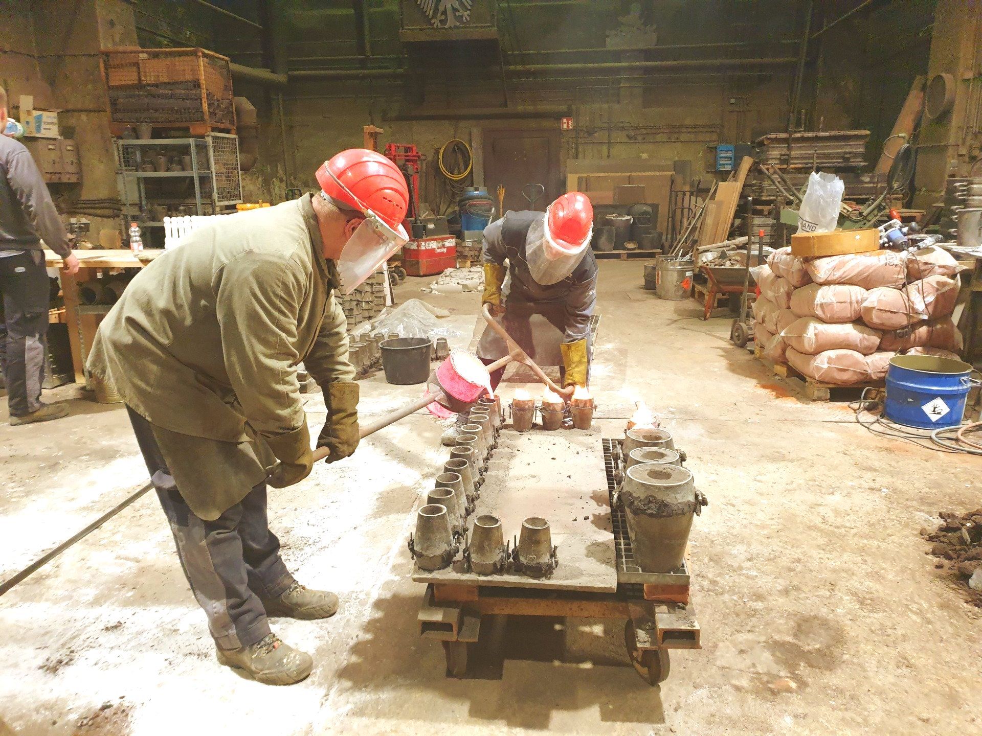 Das Bild zeigt Mitarbeiter beim Bronzeguss. Sie gießen 1160 Grad heiße, glühende Bronze in die vorbereiteten Formen.