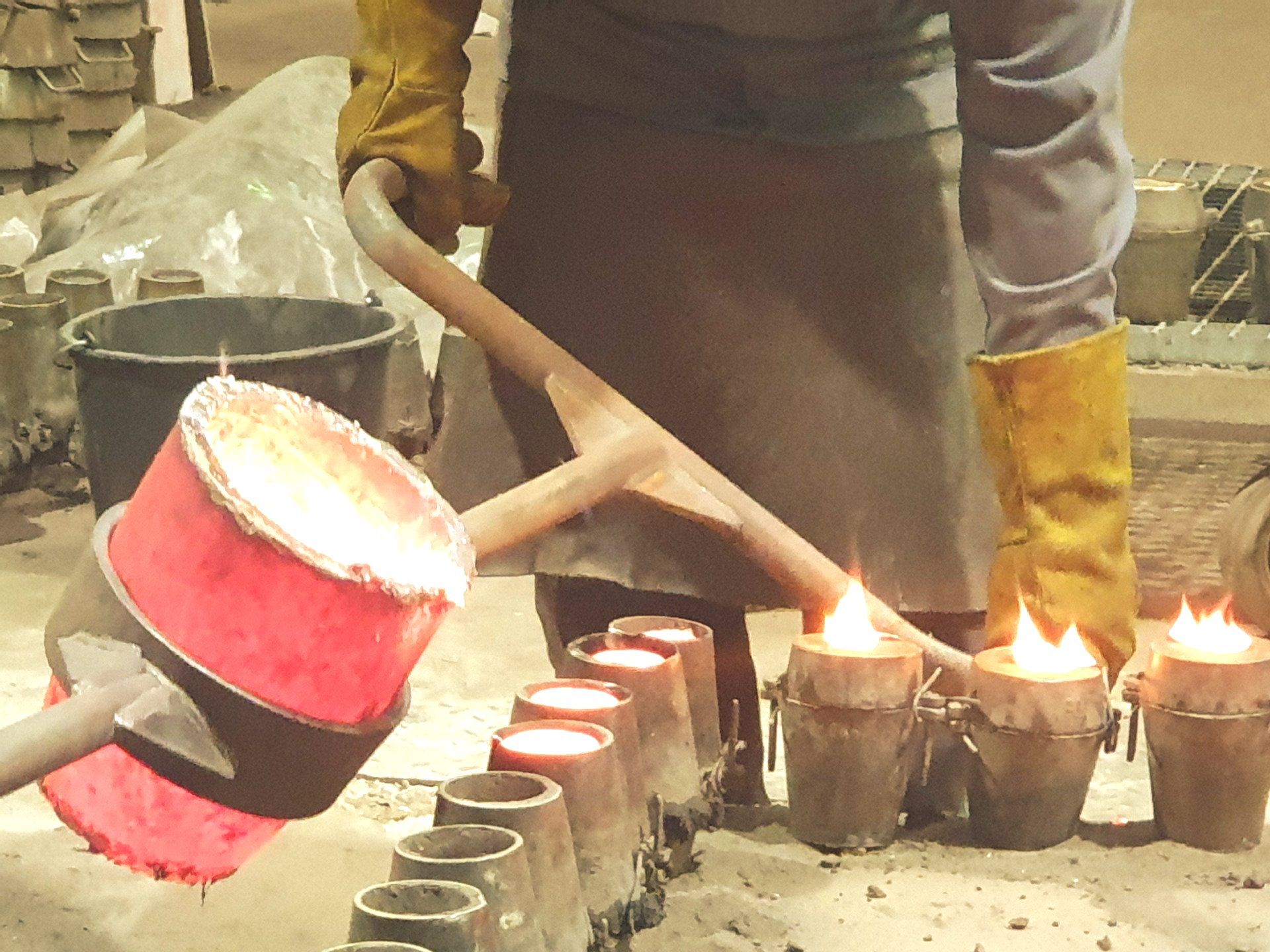 Das Bild zeigt Mitarbeiter beim Bronzeguss. Sie gießen 1160 Grad heiße, glühende Bronze in die vorbereiteten Formen.