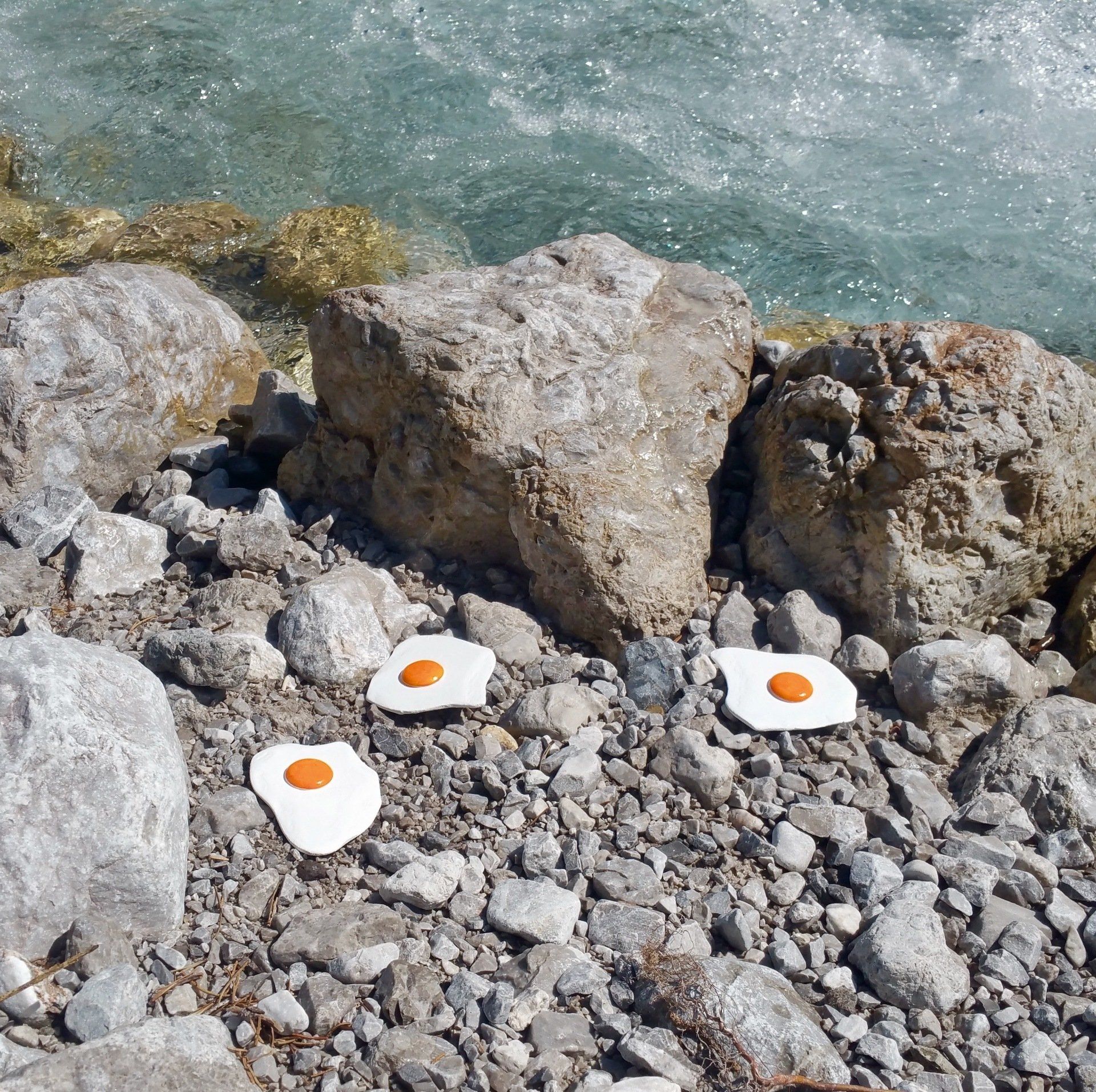 Das Bild zeigt Spiegeleier-Skulpturen von Bildhauer und Künstler Oliver Pohl aus Haste bei Wunstorf am Steinhuder Meer. Das Foto ist an einem Gebirgsbach bei Berchtesgaden entstanden.