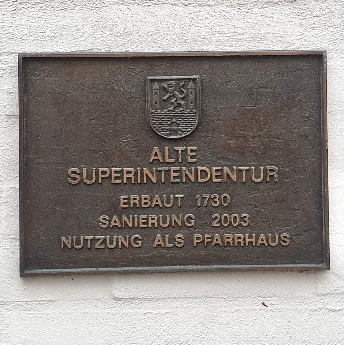 Das Bild zeigt eine Bronzetafel für ein historisches Gebäude in Neustadt am Rübenberge, gefertigt von Bildhauer Oliver Pohl