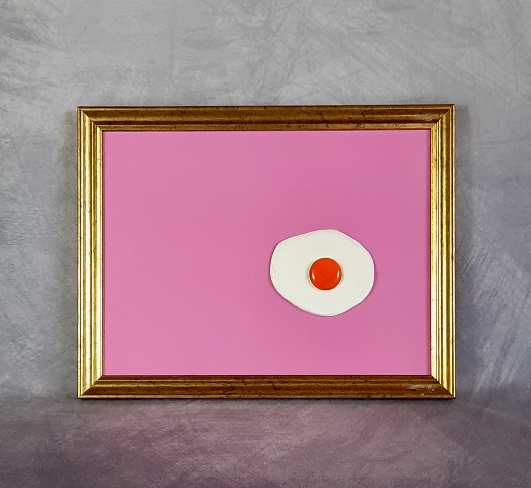 Plastisches Pop Art Spiegelei auf rosa Grund in einem goldenen Rahmen.