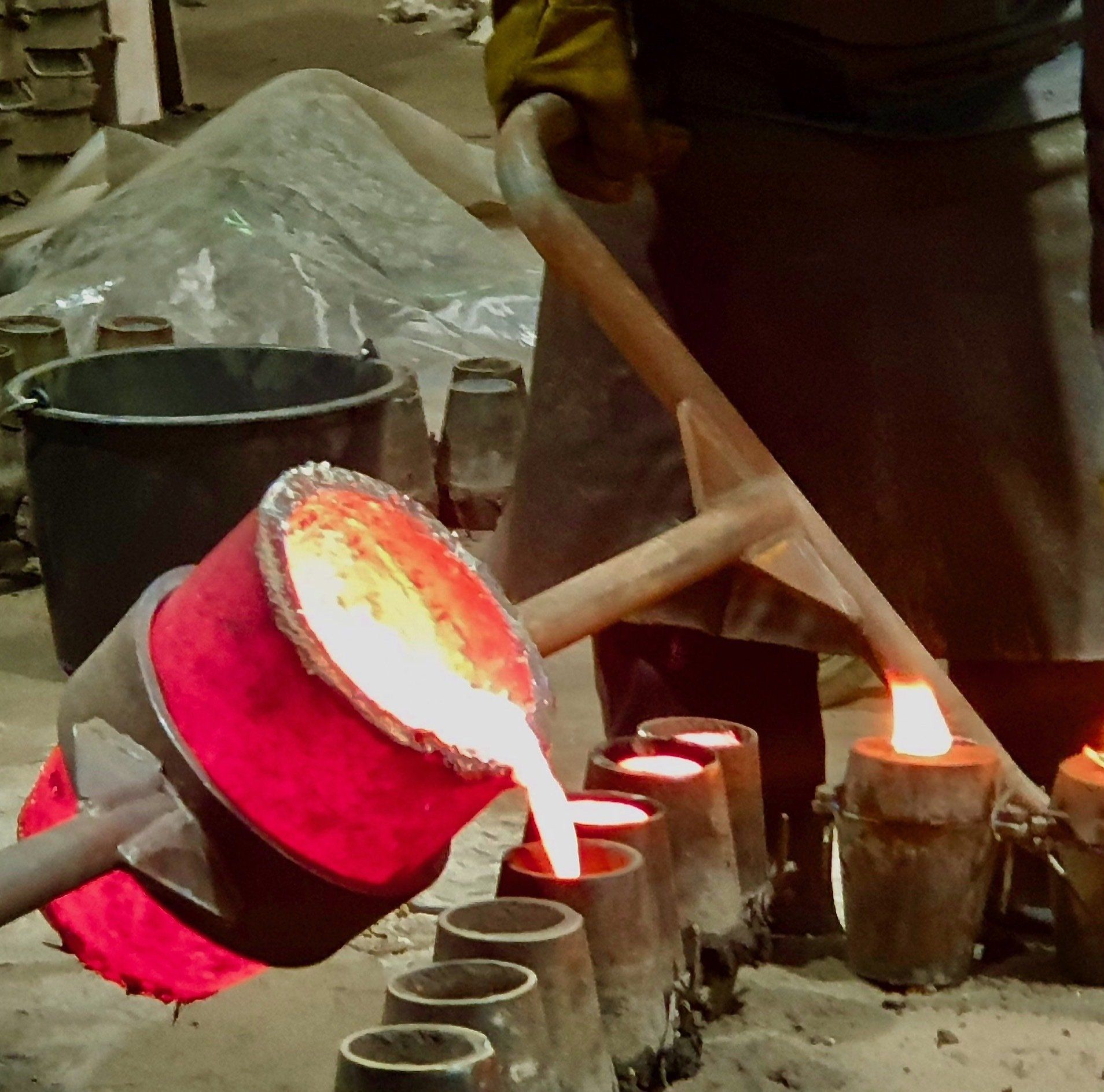 Fingerspitzengefühl - jede Form wird einzeln mit glühender Bronze befüllt Glühende Bronze aus einem Tiegel fließt in mehrere Formen und beschreibt so den Herstellungsprozess der Bronzefiguren Friends.