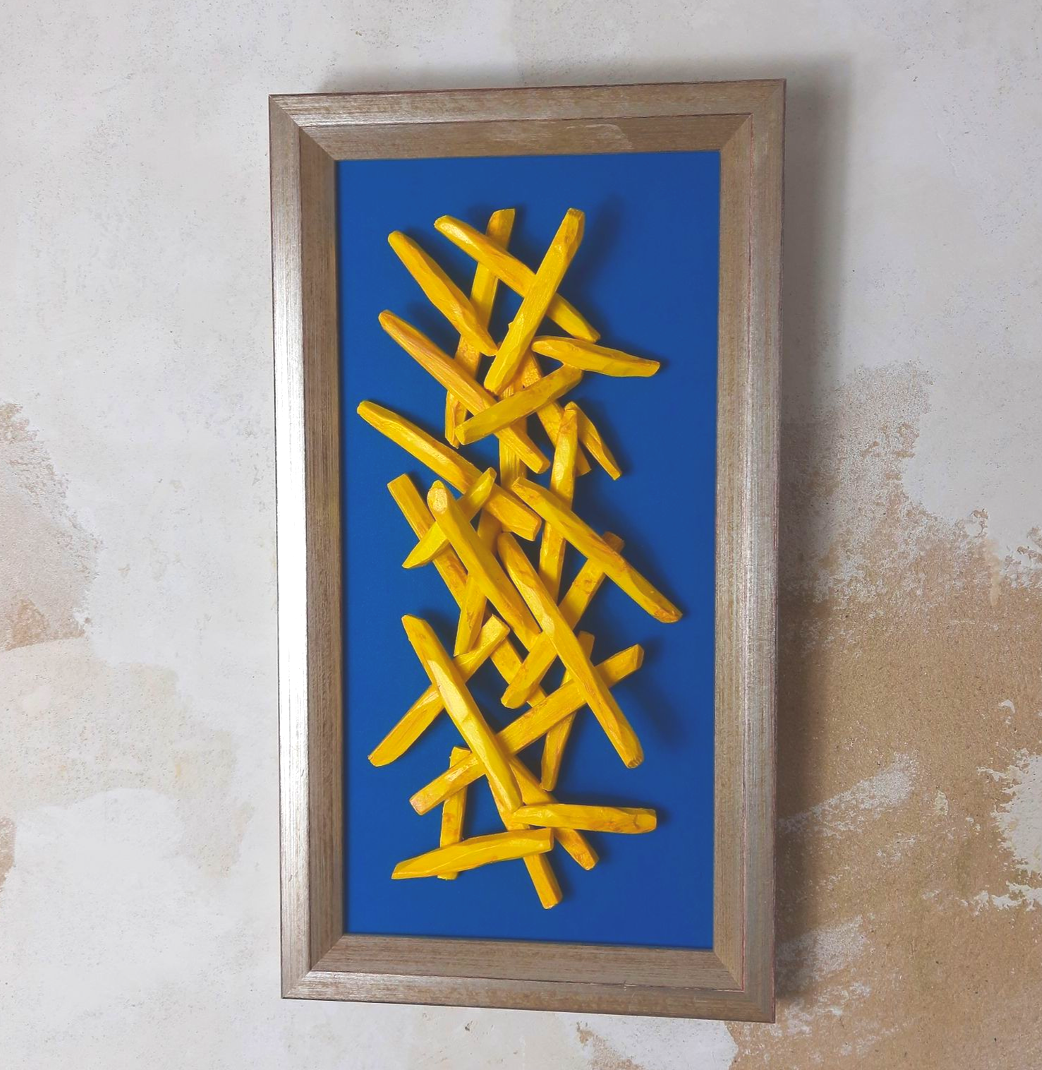 Pop-Art Fritten Bild mit plastisch gearbeiteten gelben Fritten auf einem petrolfarbenen Grund in einem silbernen Rahmen.