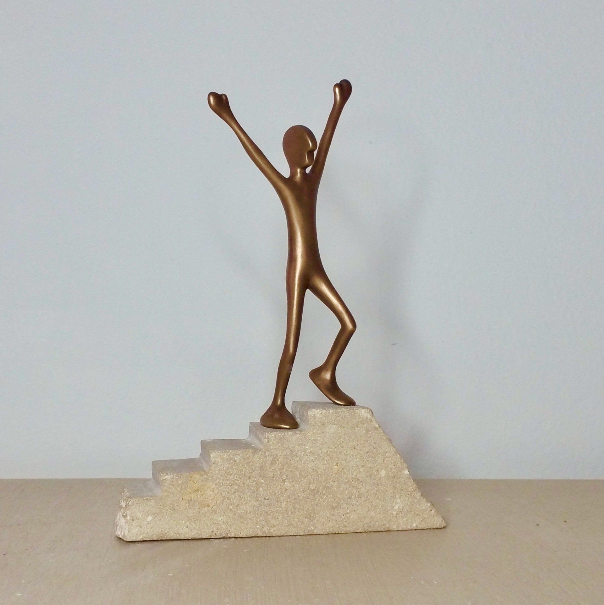 Das Bild zeigt die Bronzefigur Friend Nummer 13 in Siegerpose auf einer Steintreppe.