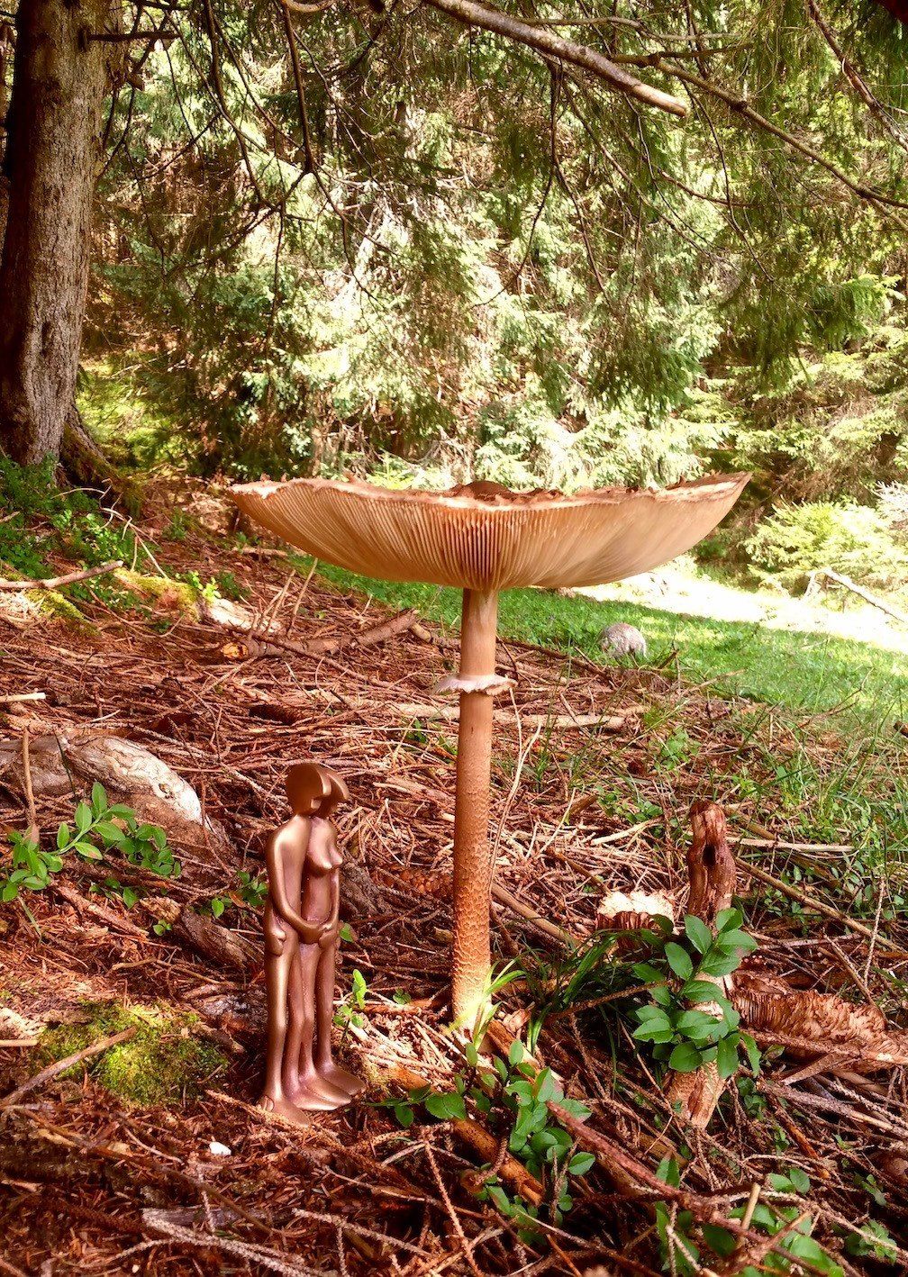 Das Bild zeigt eine Bronzefigur der Serie FRIENDs von Bildhauer Oliver Pohl aus Haste im Schaumburger Land, stehend unter einem Riesenschirmling Pilz im Wald.