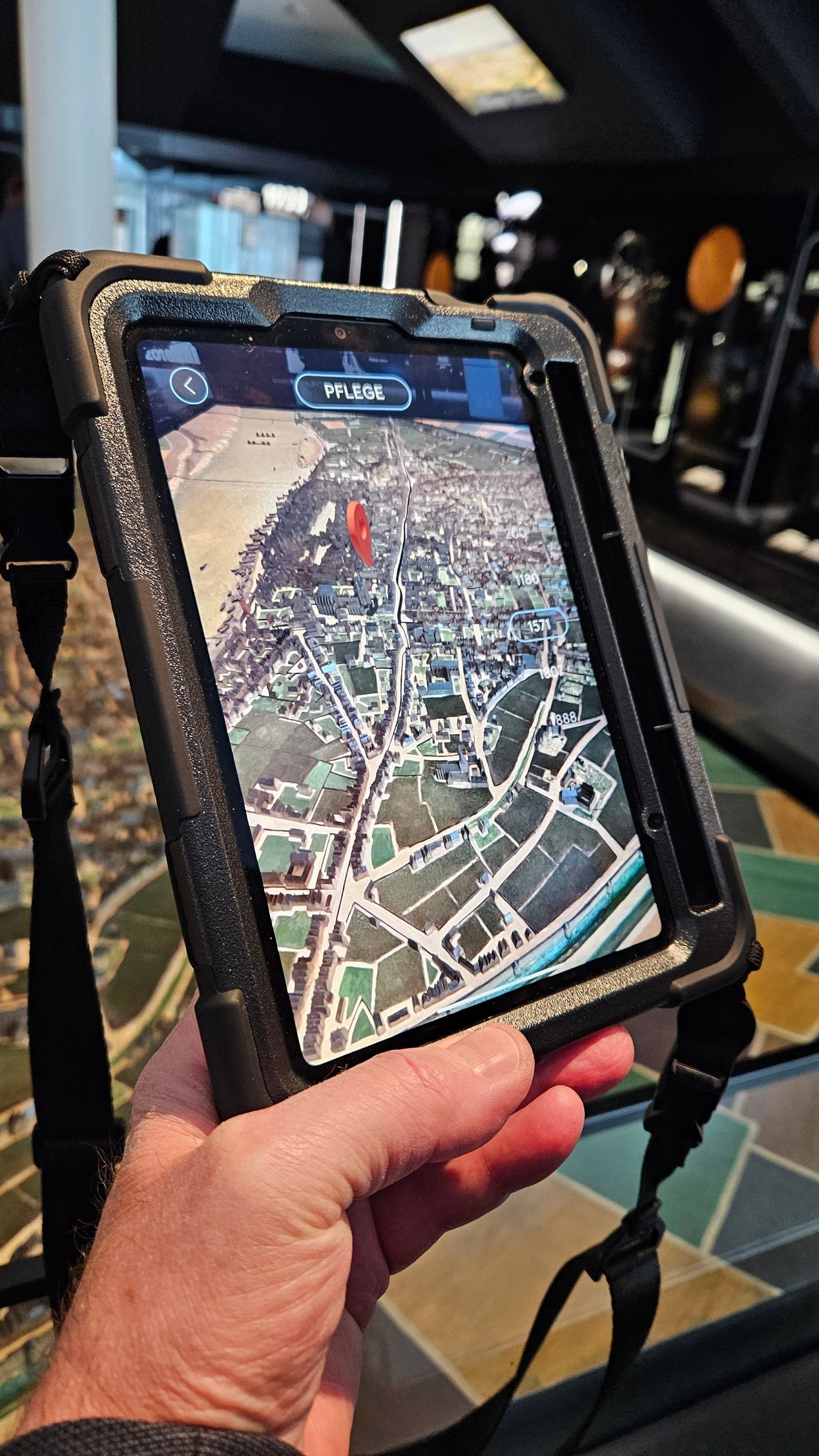 Der Schirm eines bildfüllenden Tablets zeigt im Hintergrund ein Stadtmodell. Davor ist eingeblendet ein seltsames kompaktes Objekt das metallisch glänzt und aus verschiedenen Kugelformen besteht. Auf manchen sind spitze Zacken. Rechts eine Zeitleiste mit Jahreszahlen - 1571 weiß umrandet.