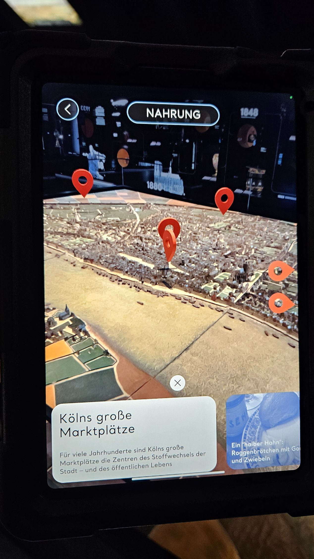 Ein Tabletbildschirm mit einem Ausschnit eines Stadtmodells. In der Mitte in ovalem Rahmen das Wort