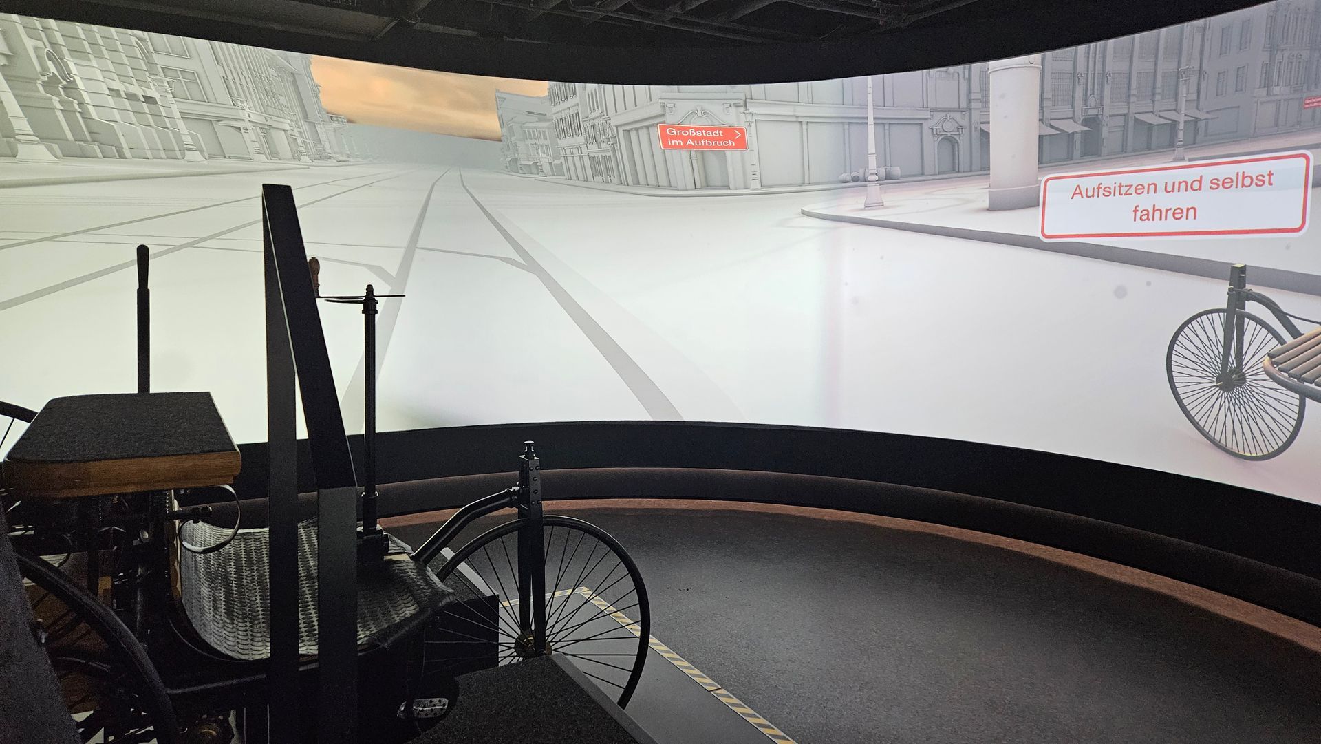 Ein Raum mit einem Teil eines alten Wagens vorne und einer gebogenen Panorama-Projektion an der Wand hinten.