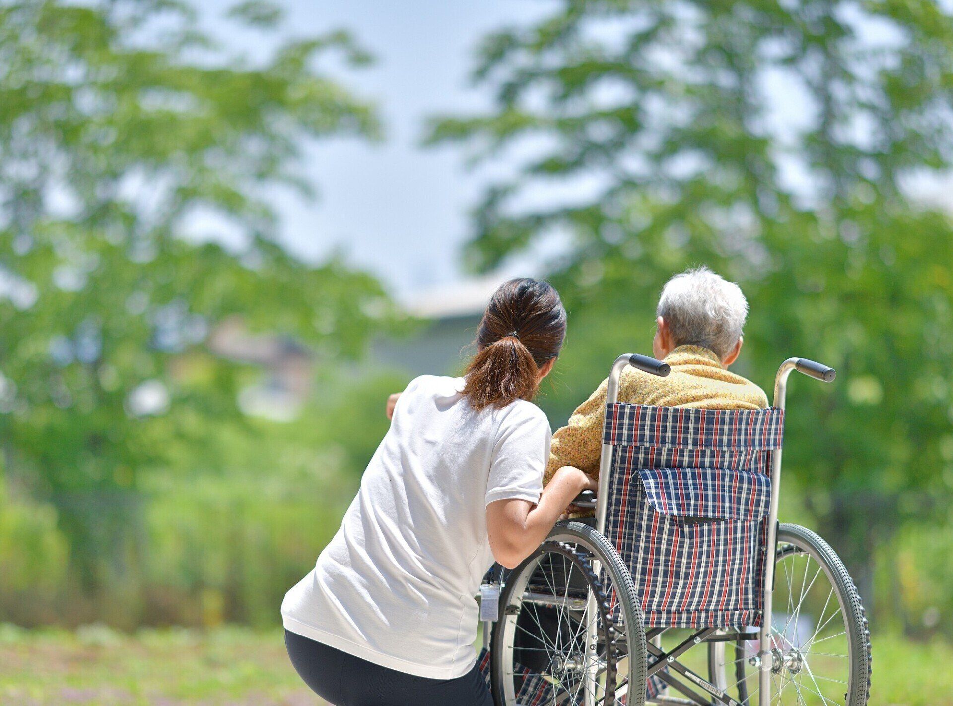 Frau kniet neben einer Seniorin im Rollstuhl Frau kniet neben einer Seniorin im Rollstuhl