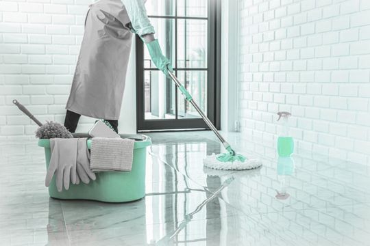 Eine Reinigungskraft die gerade einen Boden nass reinigt.