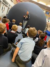 Science Dome UK presenter educating pupils about science topics inside a school in the UK with a planetarium set up at the back.