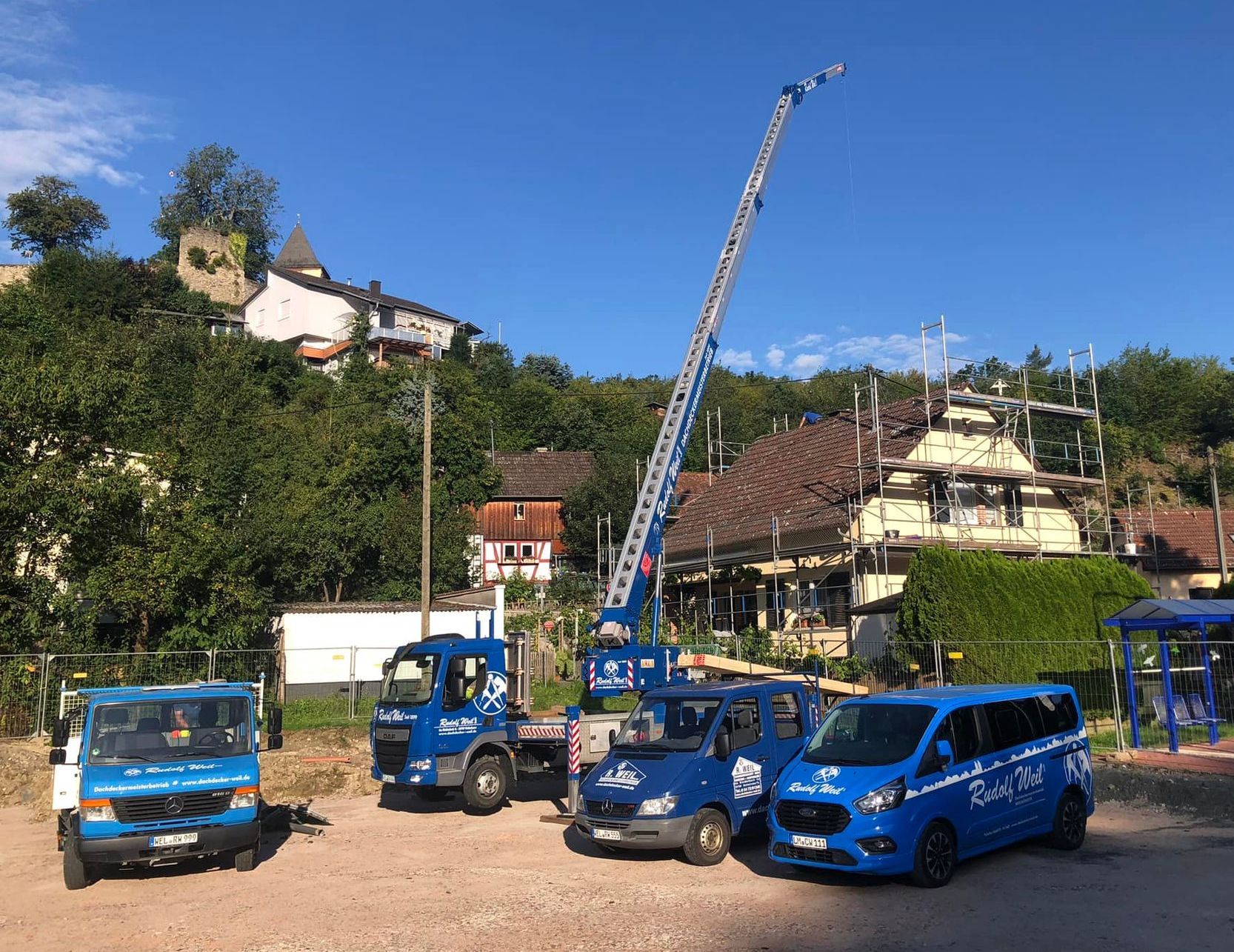 Der Fuhrpark von Dachdecker Weil mit dem ausgefahrenen Kran an einer Baustelle.