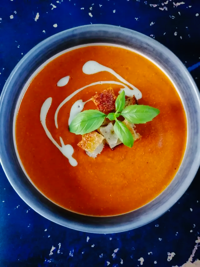 a bowl of tomato soup topped with bread croutons fresh basil and a swirl of cream