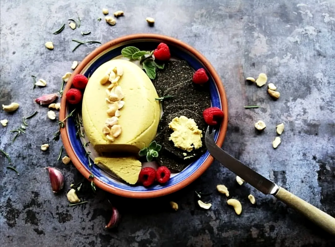 vegan cheese on a platter with black crackers and raspberries