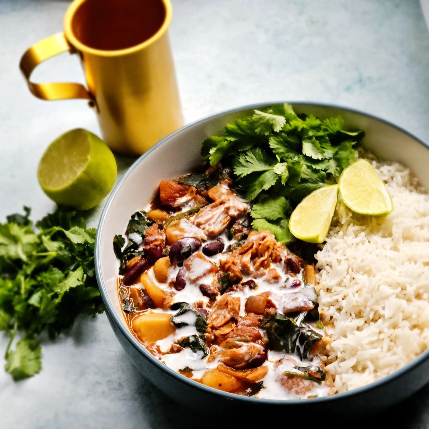 Jamaican Jerk Jackfruit and red bean stew in a bowl with rice, fresh coriander, and sliced lime wedges