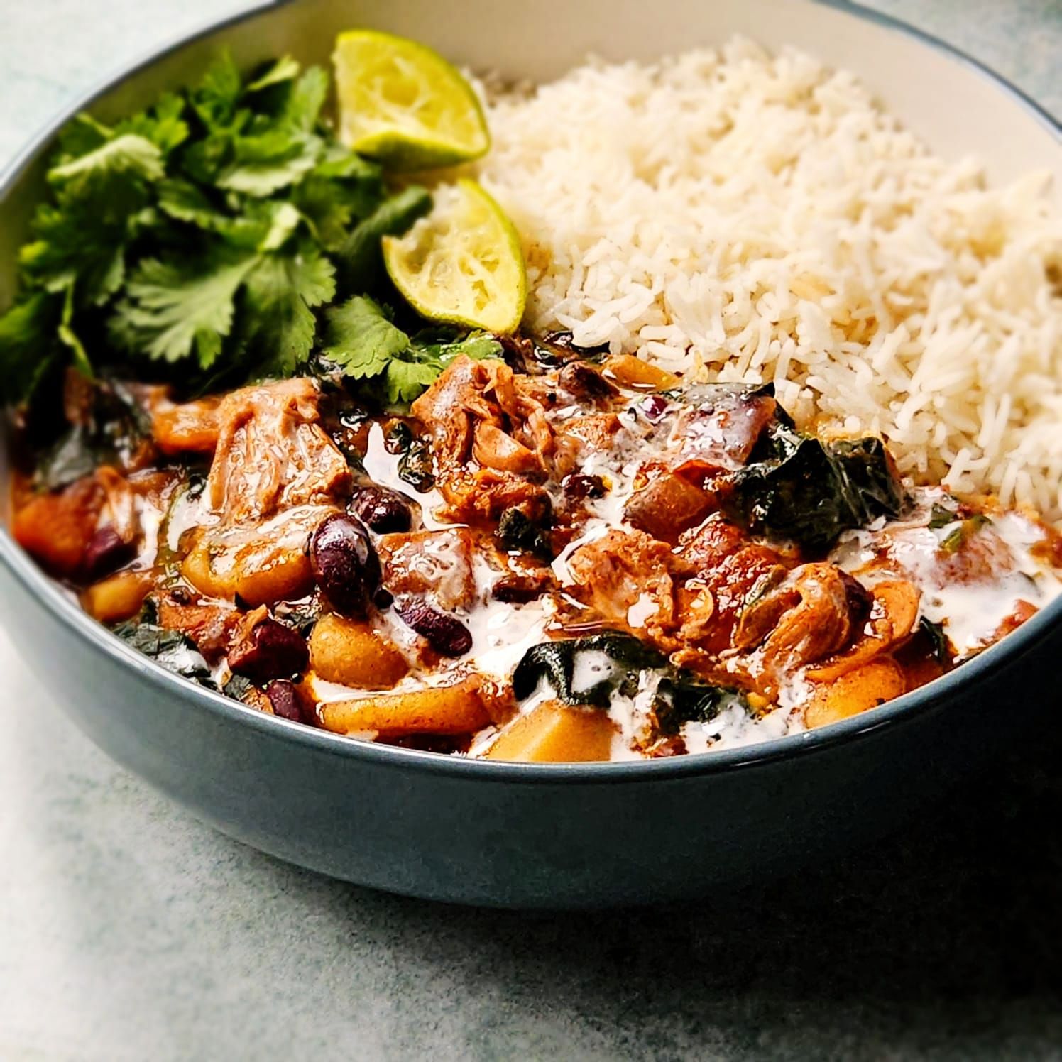 Jamaican Jerk Jackfruit and red bean stew in a bowl with rice, fresh coriander, and sliced lime wedges