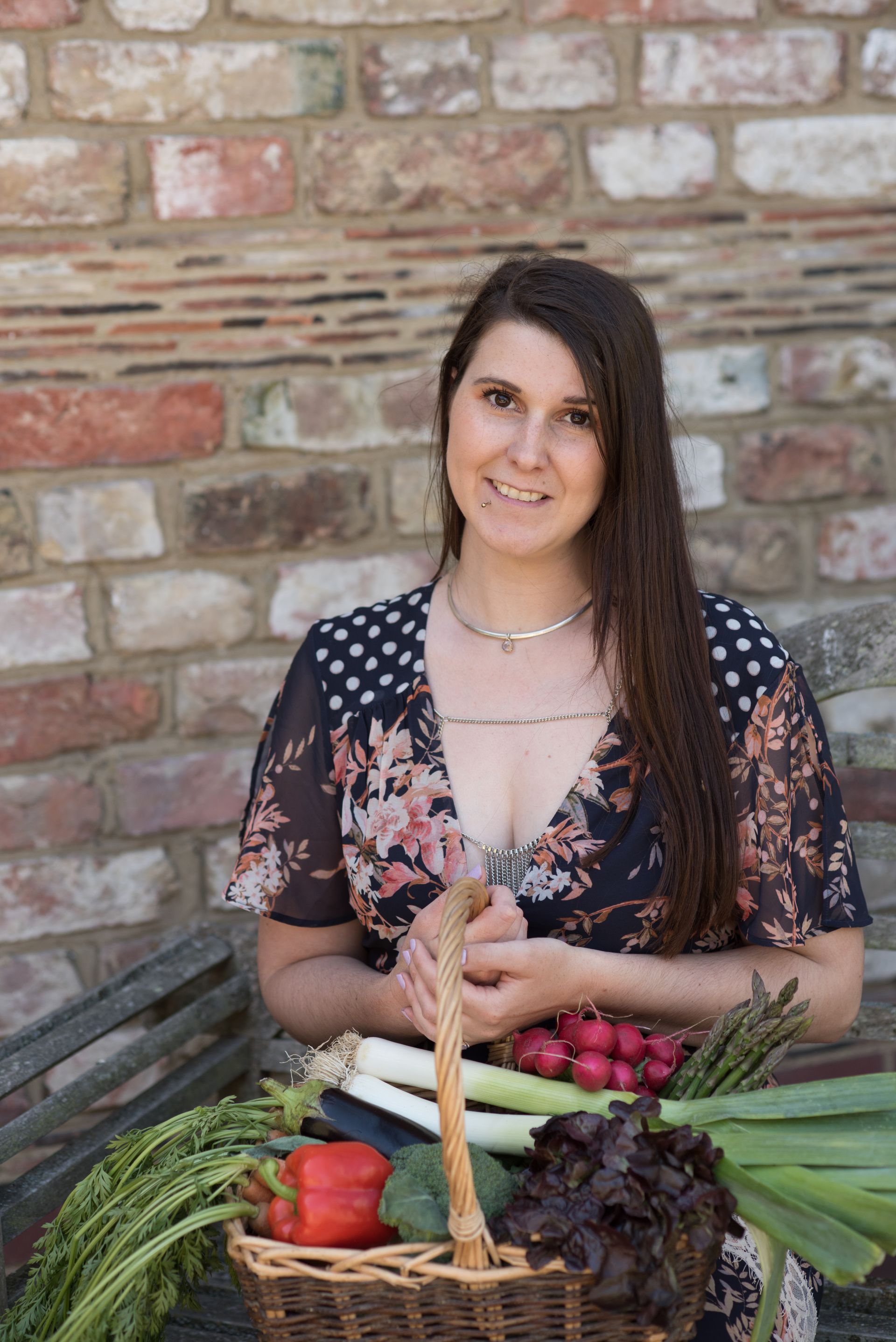Picture of rose wyles the vegan nutritionist leaning against a tree holding a basket of fresh vegetables